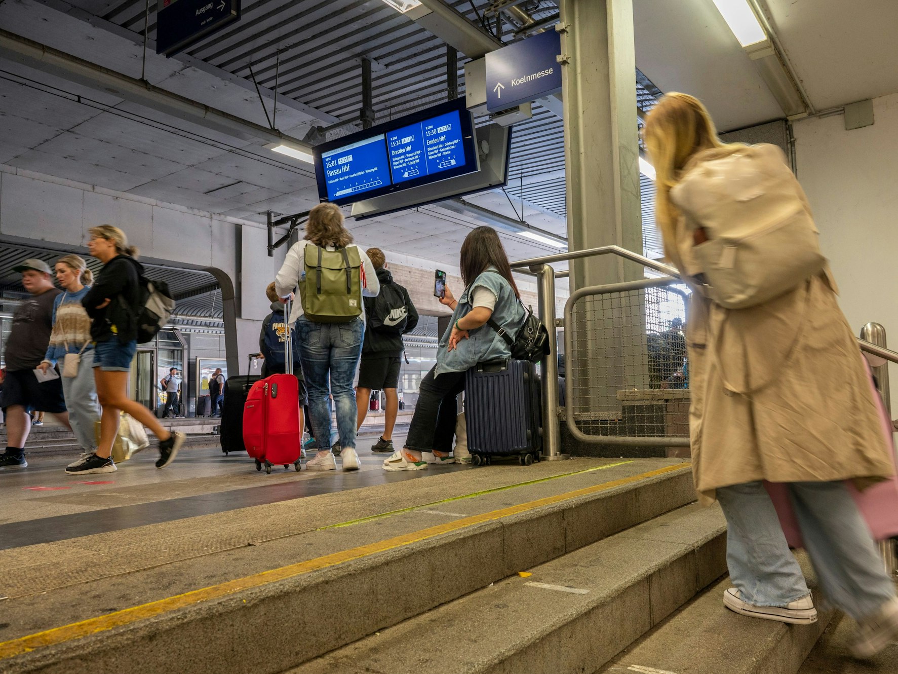 Mehrere Männer und Frauen gehen mit ihrem Gepäck durch den Bahnhof Köln Messe/Deutz.