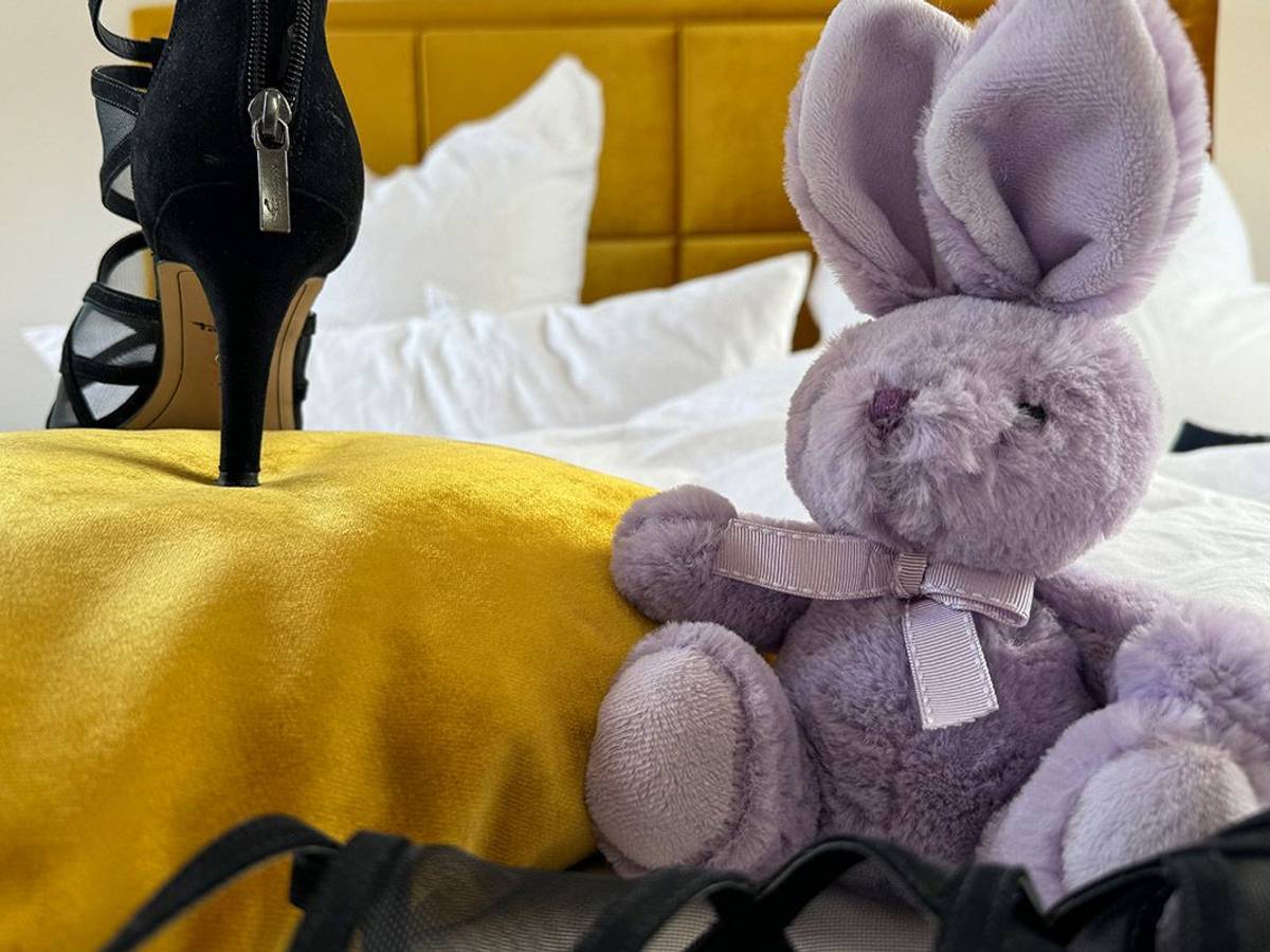 High Heels und lila Kuscheltier Hase nebeneinander auf einem Bett.
