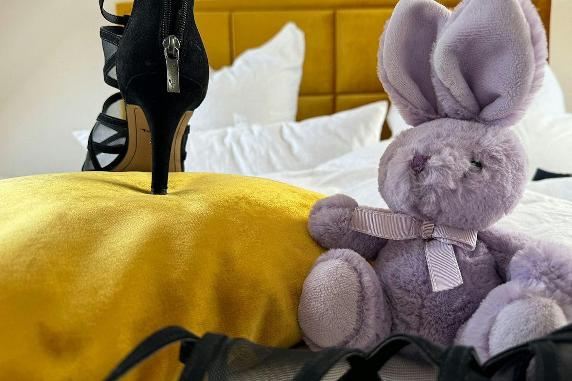 High Heels und lila Kuscheltier Hase nebeneinander auf einem Bett.
