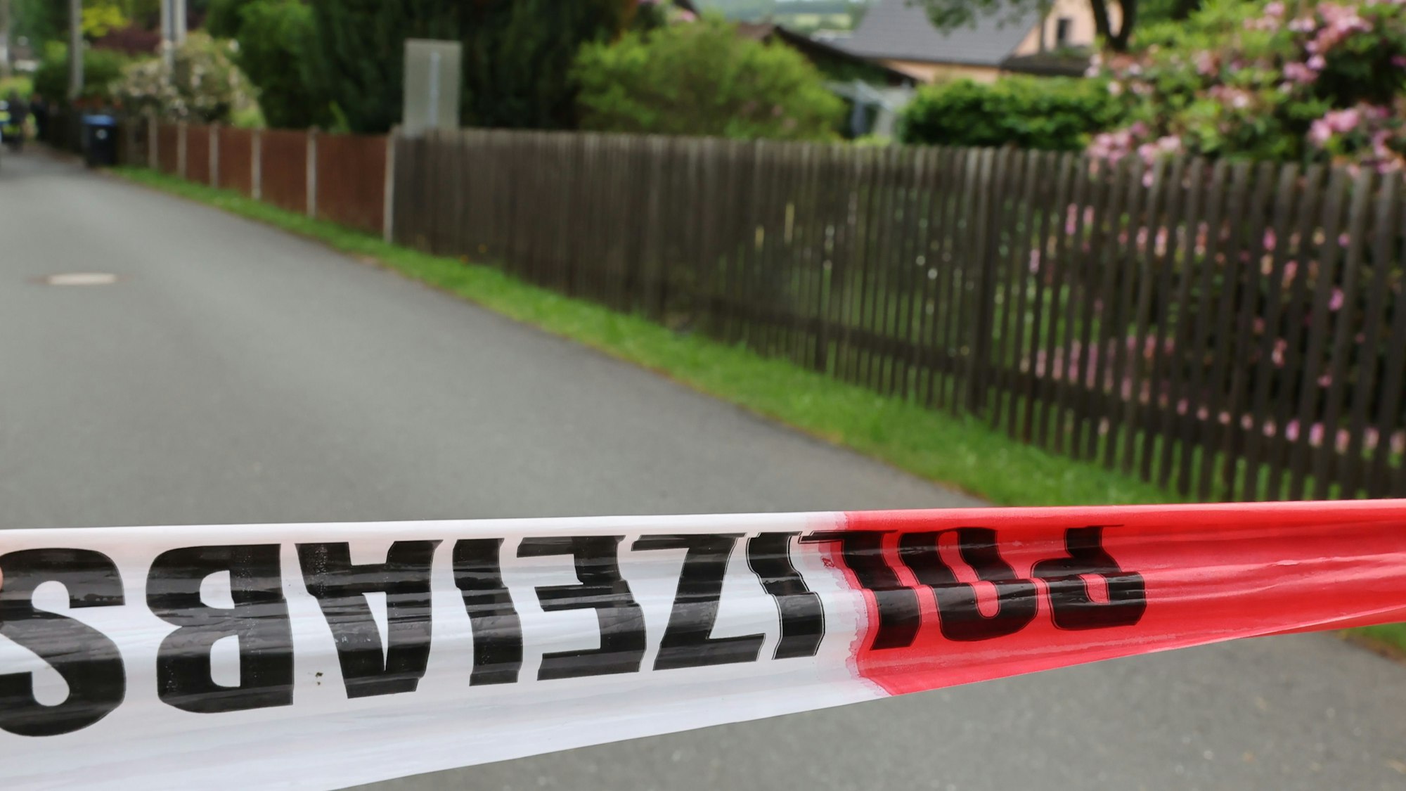 Ein Band mit der Aufschrift „Polizeiabsperrung“ sichert einen Tatort. Dahinter sind kleine Gärten zu sehen.