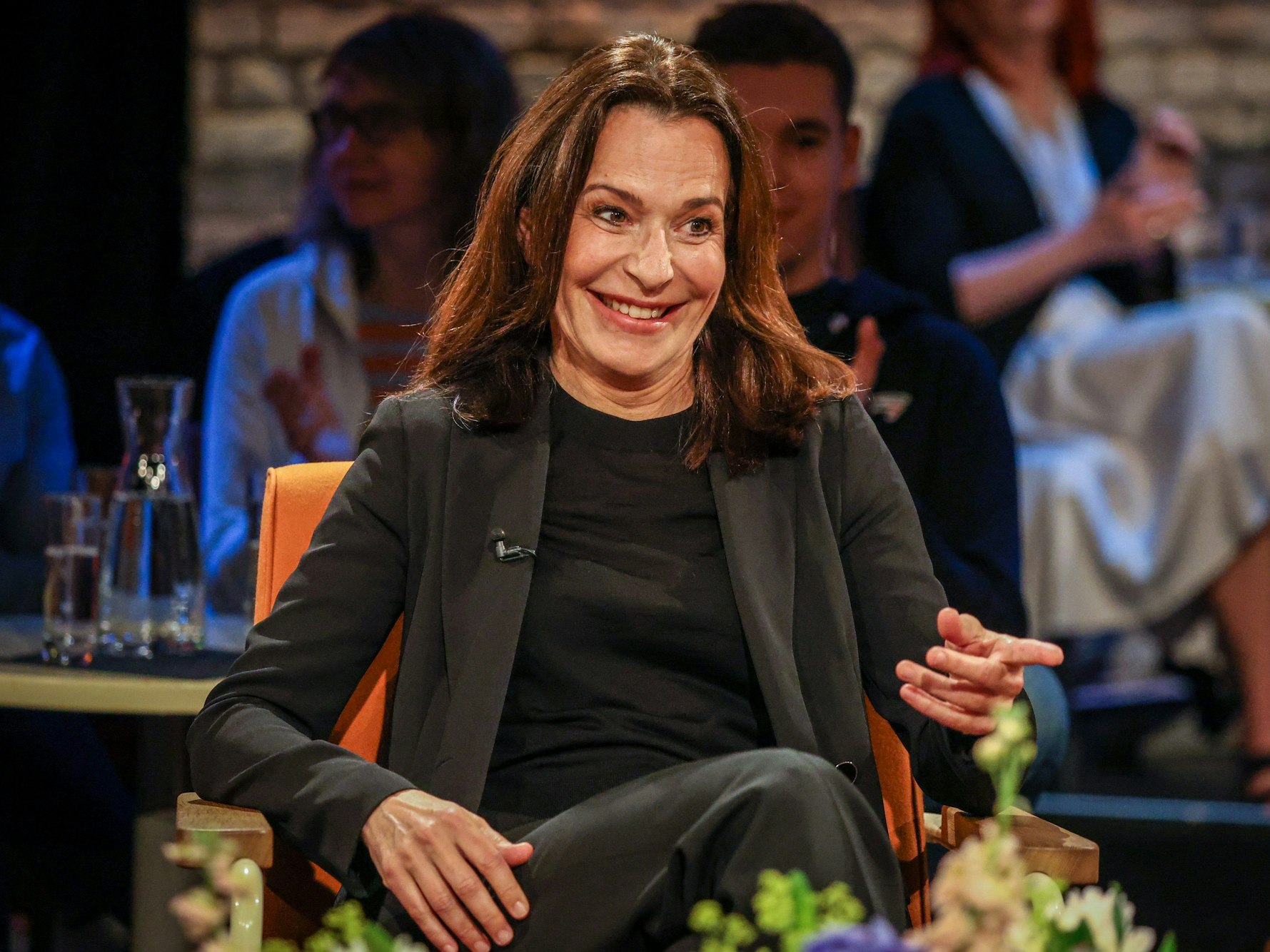 Moderatorin Anne Will sitzt in einem TV-Studio auf einem Stuhl und lächelt.