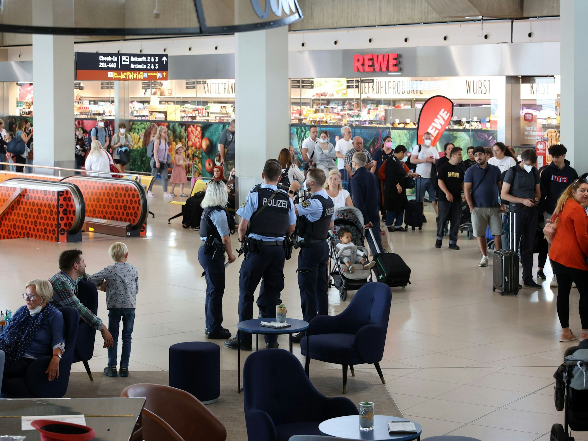 Menschen gehen durch den Flughafen Köln/Bonn, auch eine Streife der Bundespolizei ist zu sehen.