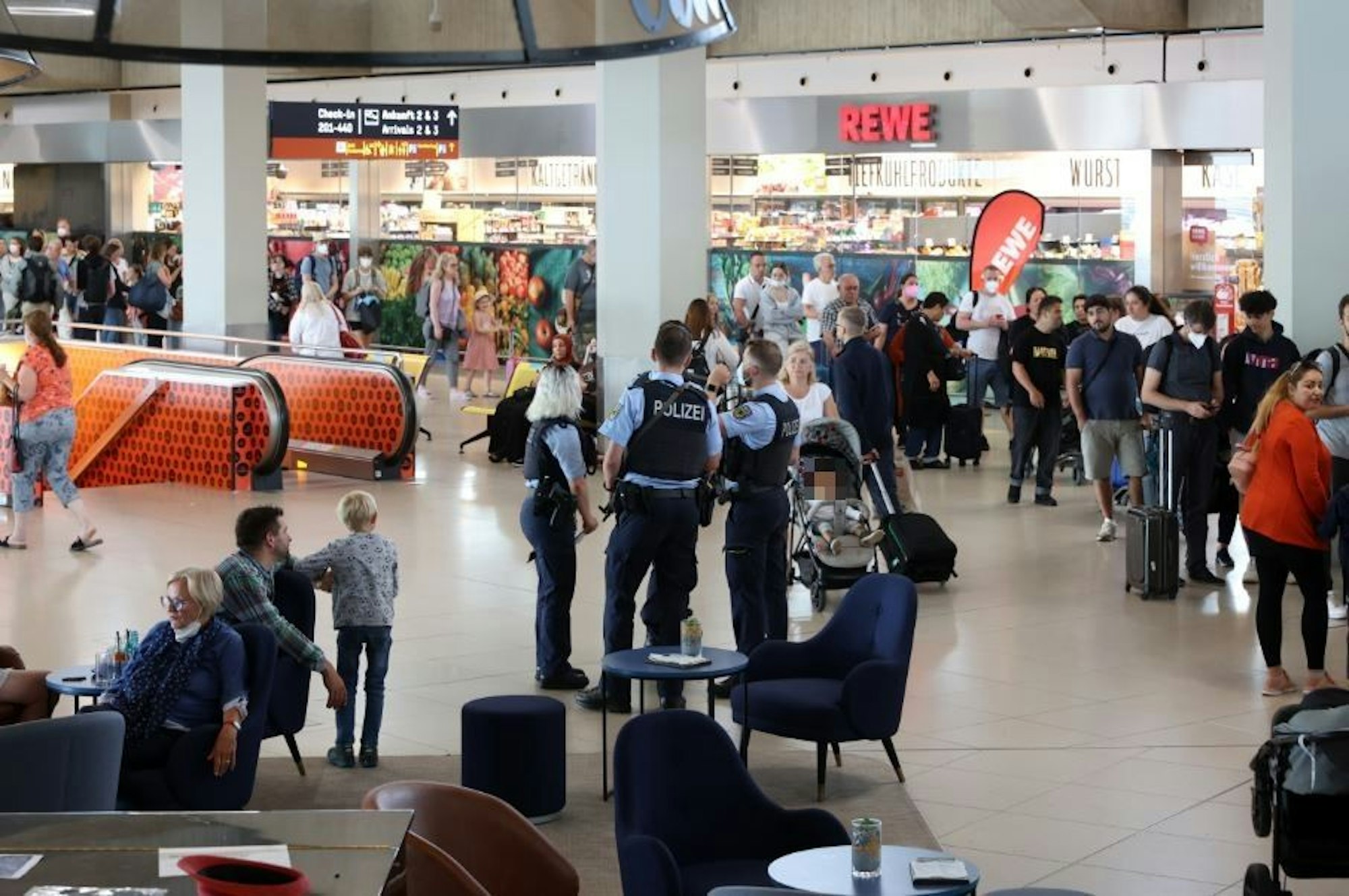 Menschen gehen durch den Flughafen Köln/Bonn, es sind auch Polizisten zu sehen.