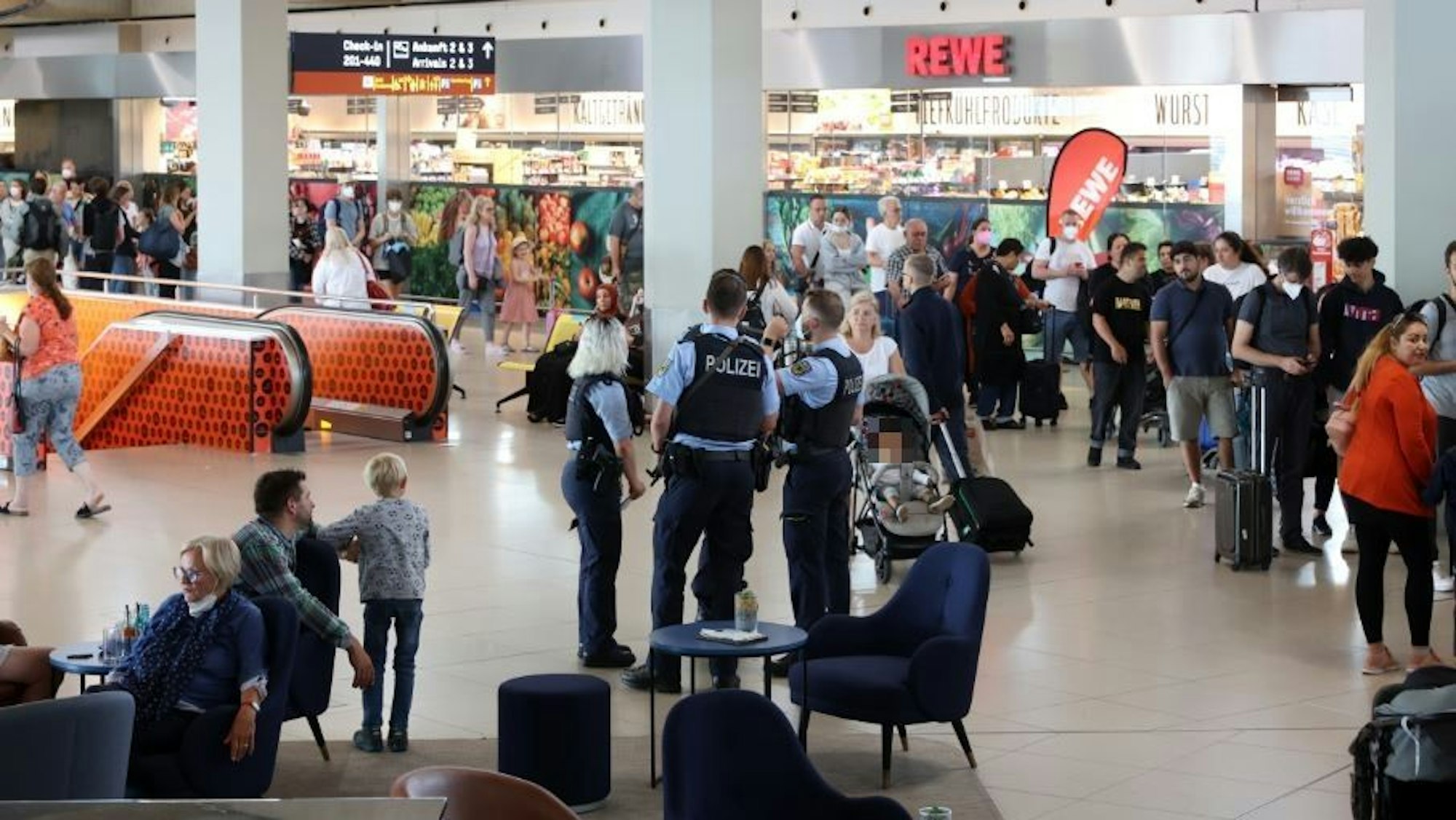 Menschen gehen durch den Flughafen Köln/Bonn, es sind auch Polizisten zu sehen.