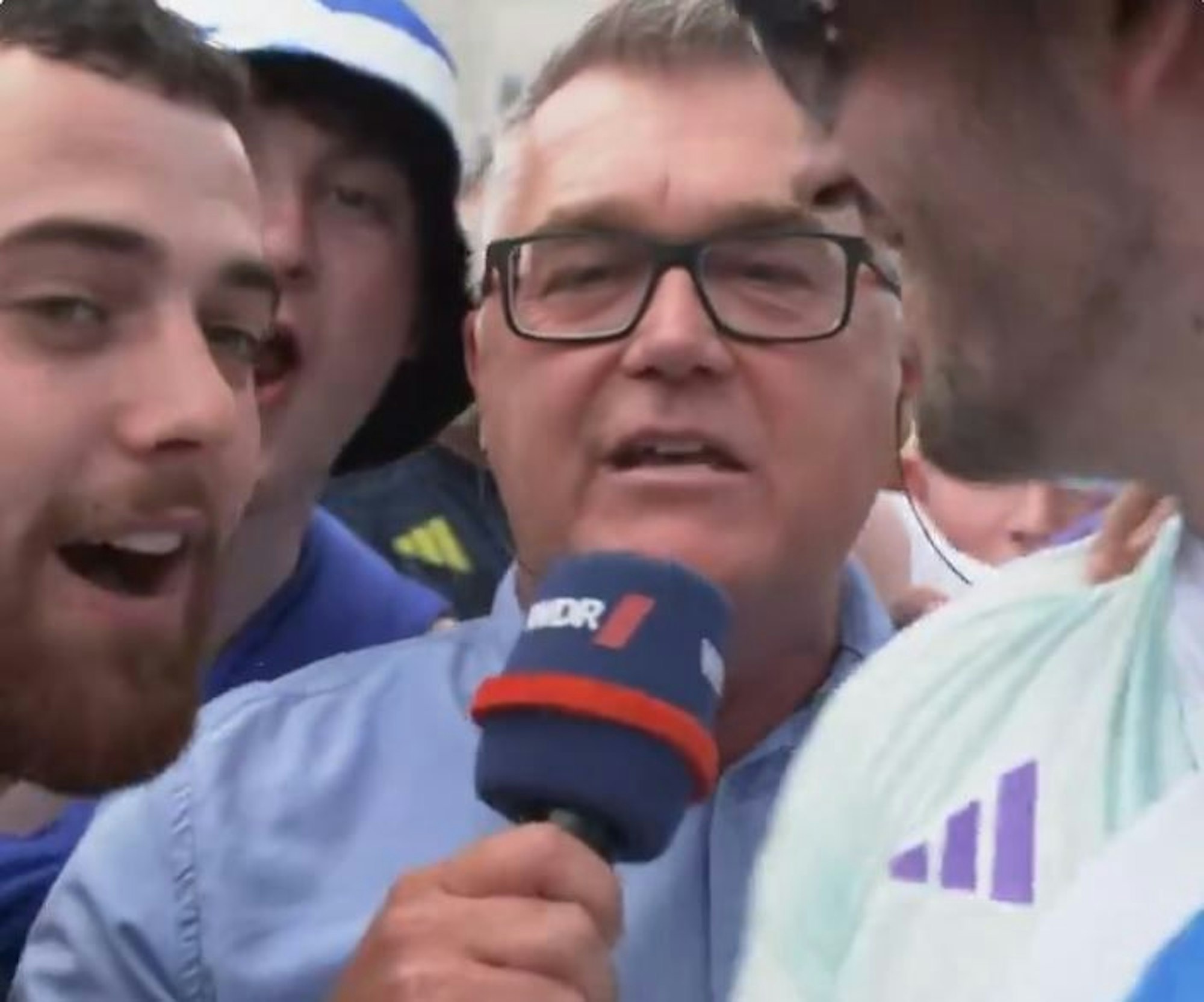 Ein Reporter des WDR steht im Pulk von schottischen Fans in Köln und spricht in sein Mikrofon.