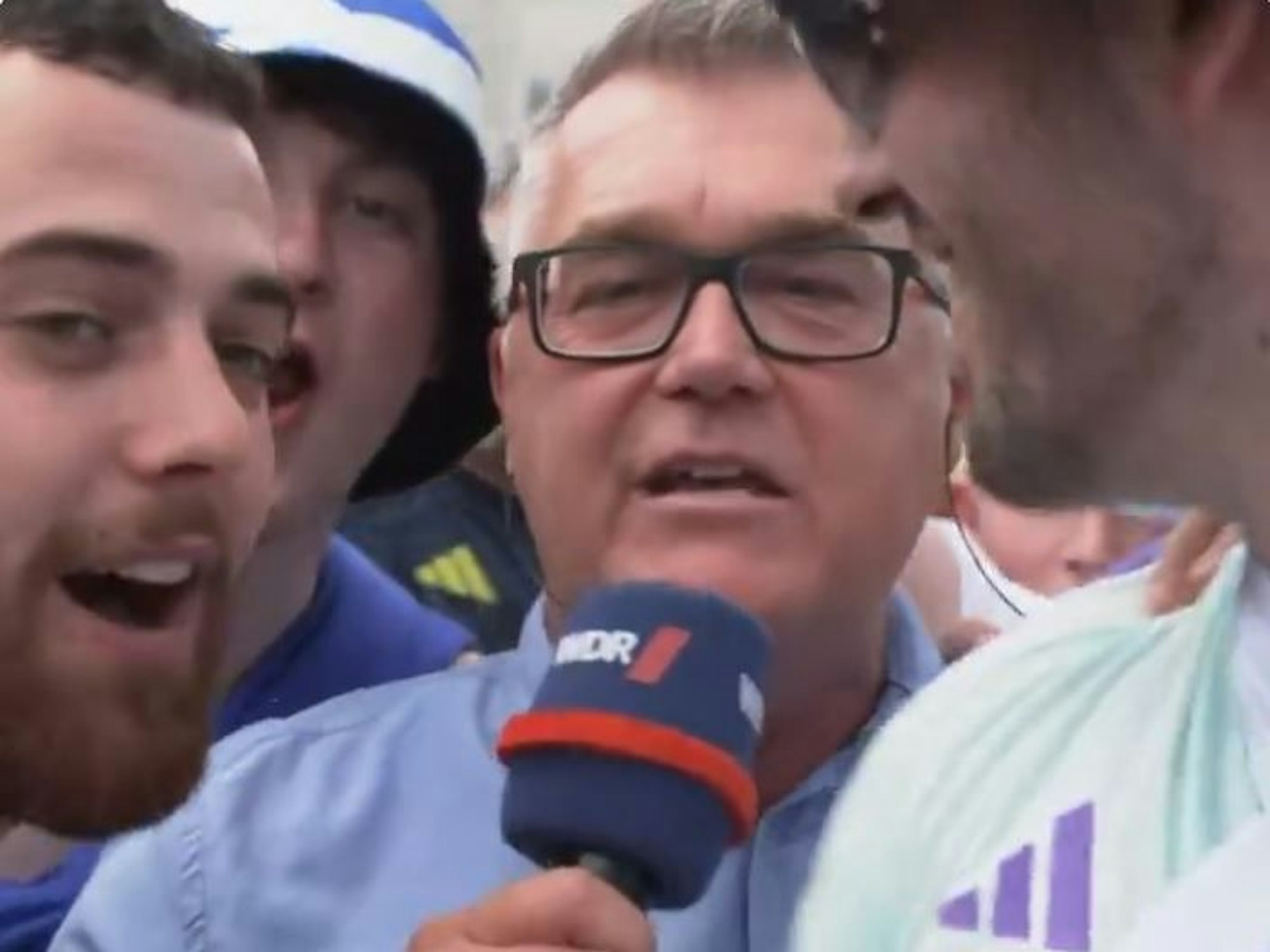 Ein Reporter des WDR steht im Pulk von schottischen Fans in Köln und spricht in sein Mikrofon.