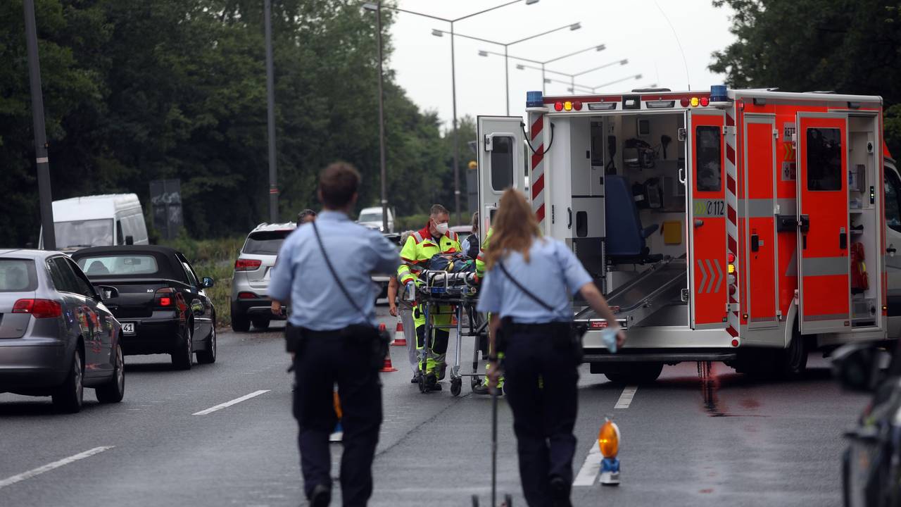 Ein Rettungswagen steht auf einer Straße, zwei Einsatzkräfte der Polizei nehmen Unfallspuren auf.