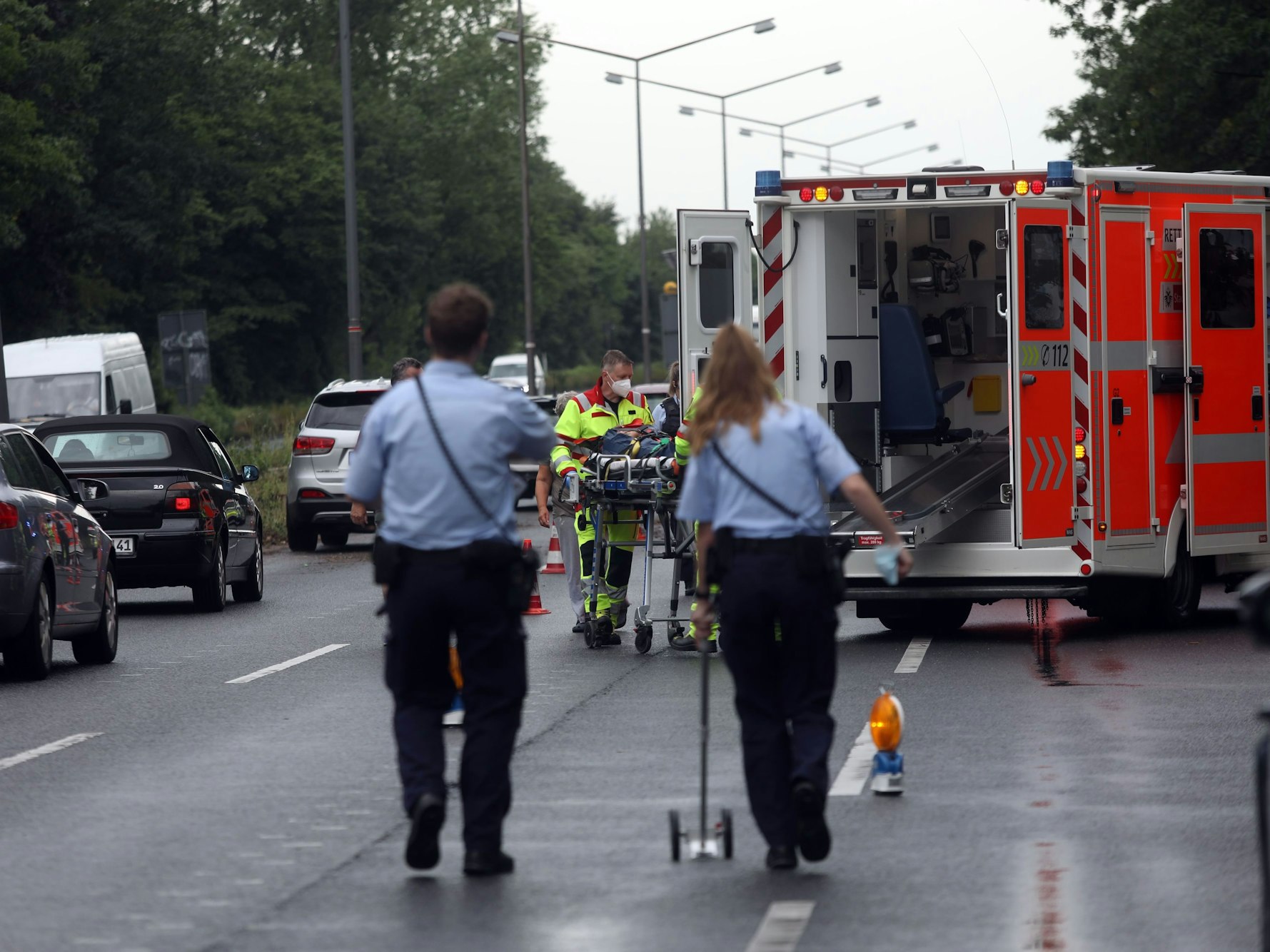 Zwei Polizeikräfte sichern auf einer Fahrbahn Spuren, vor ihnen steht ein Rettungswagen.