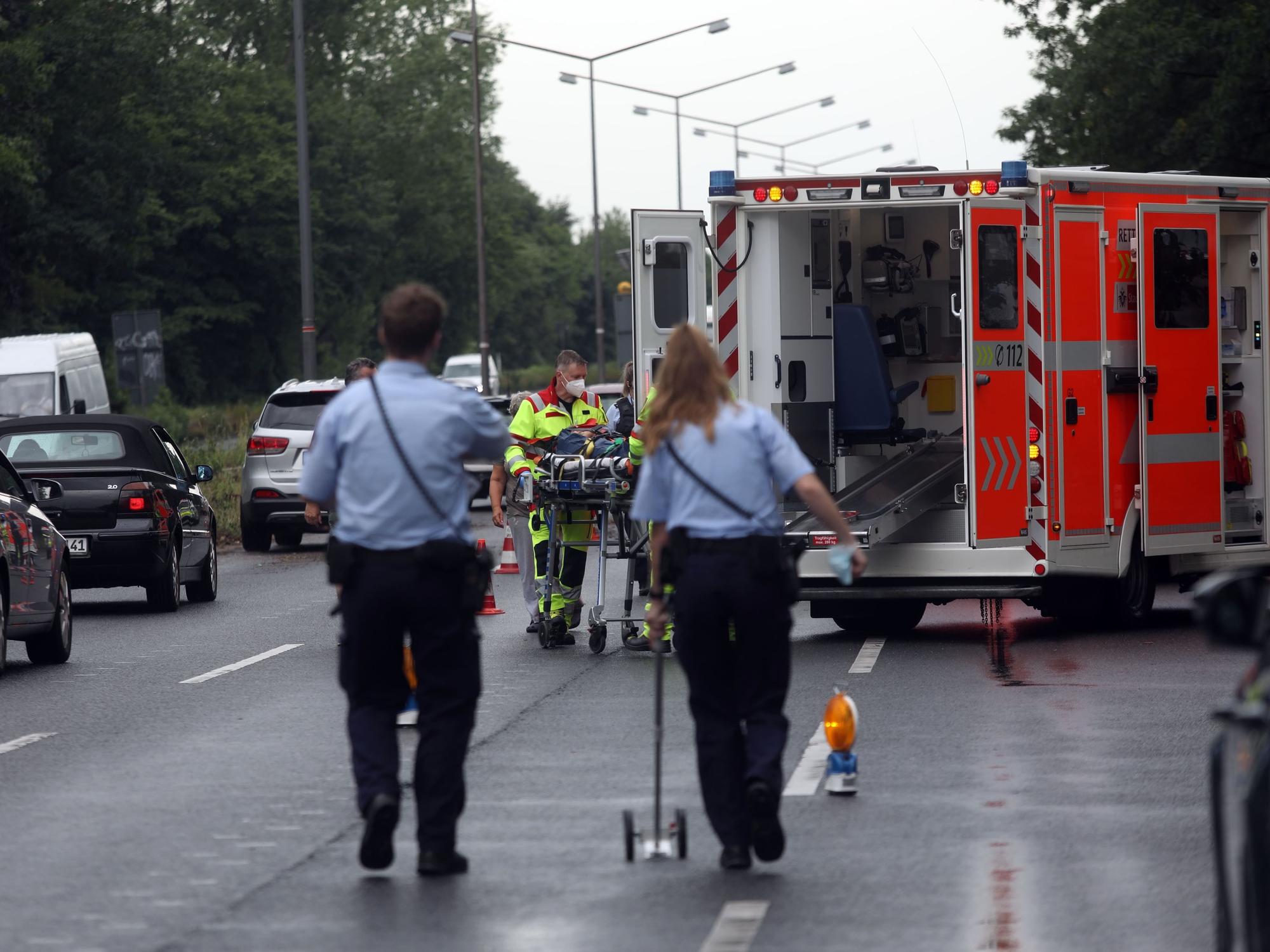 Zwei Polizisten und ein Rettungswagen an einer Unfallstelle in Köln, nebenher fährt der Verkehr an der Unfallstelle vorbei.