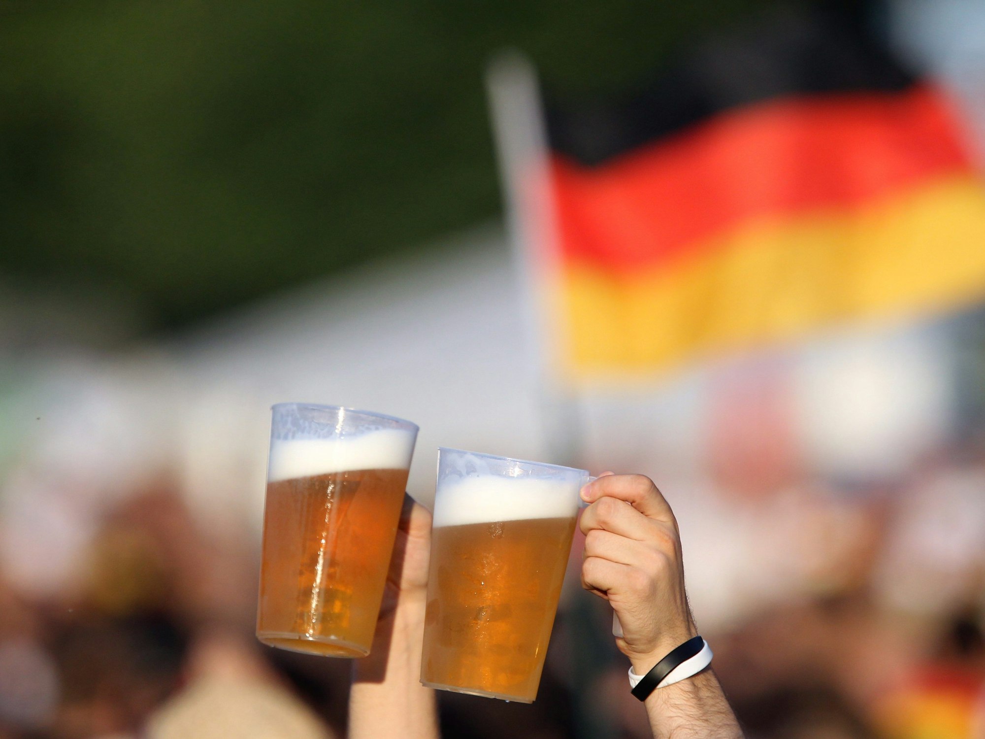 Zwei volle Bierbecher vor einer Deutschland-Fahne.