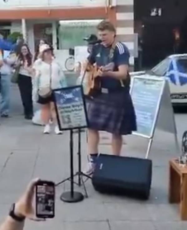Ein Schottland-Fan steht in Köln mit Gitarre auf der Straße.