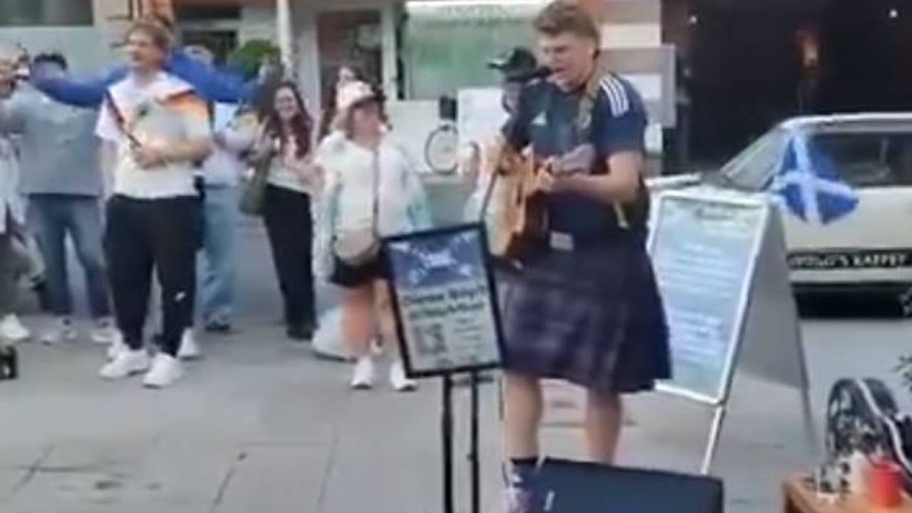 Ein Schottland-Fan steht in Köln mit Gitarre auf der Straße.