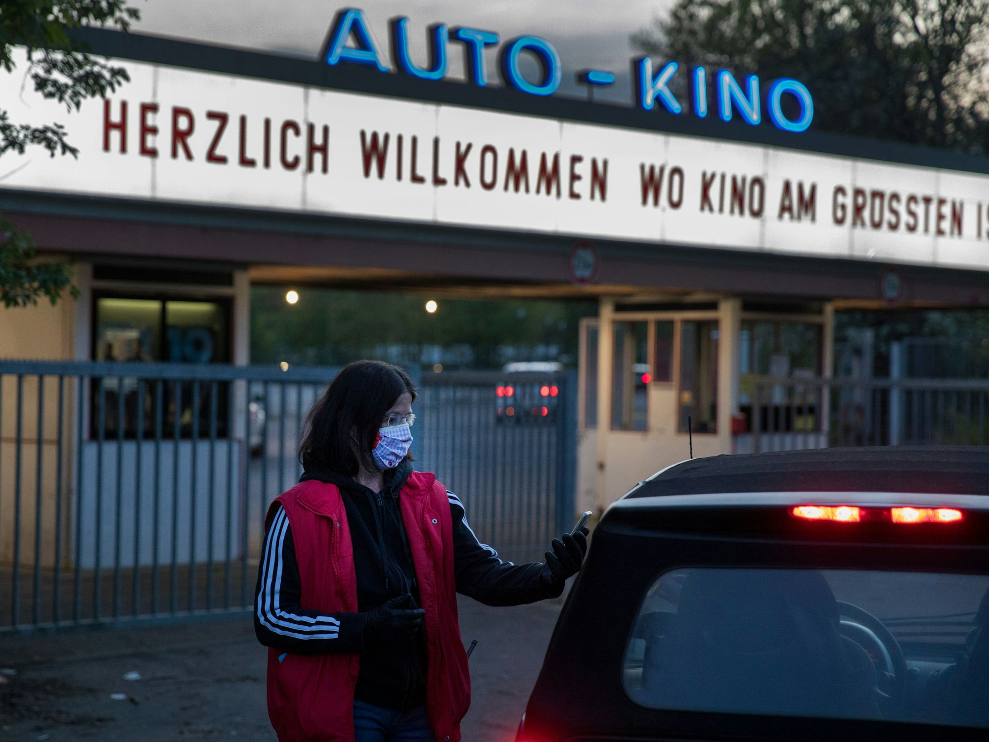 Mitarbeiterin des Kölner Autokinos steht an einem Auto und kontrolliert die Eintrittskarten.