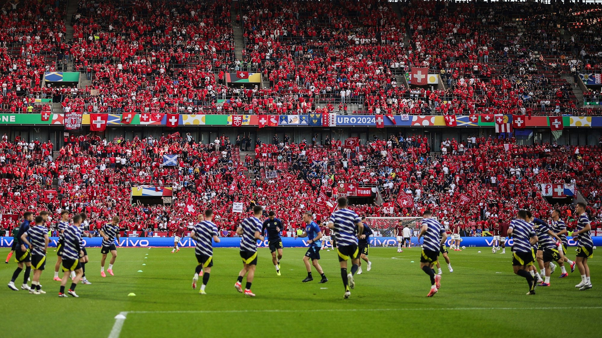 Schottische Spieler laufen sich im Rhein-Energie-Stadion warm, Fans aus der Schweiz stehen auf der Tribüne.