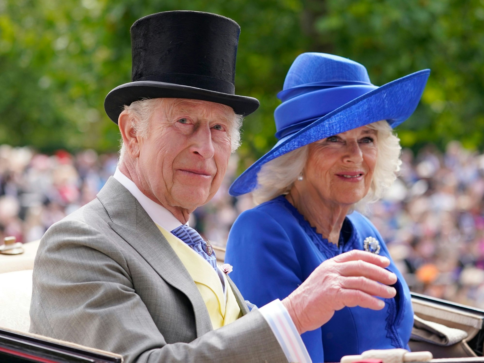 König Charles III. (l) und Königin Camilla winken bei ihrer Ankunft in der Kutsche am ersten Tag des Royal Ascot Pferderennens auf der Rennbahn in Ascot.