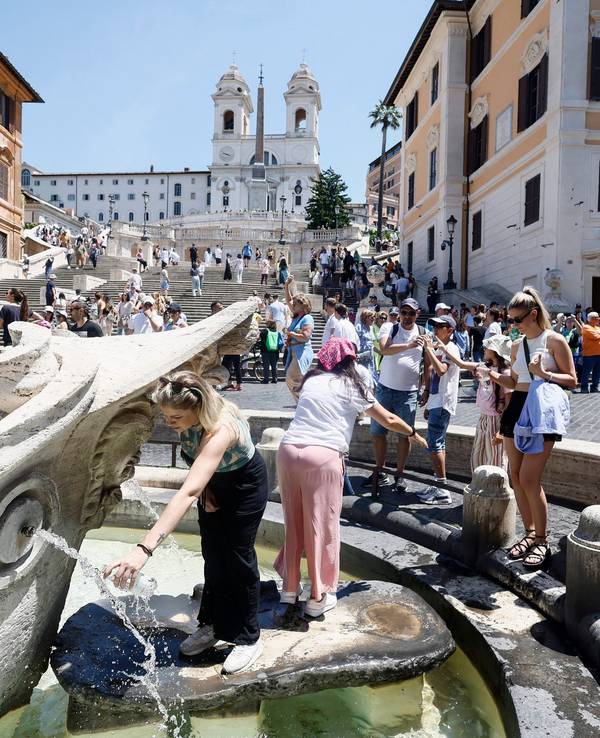 Menschen stehen an einem Brunnen an, um sich an dem heißen Tag auf der Piazza di Spagna in Rom unterhalb der Spanischen Treppe zu erfrischen.