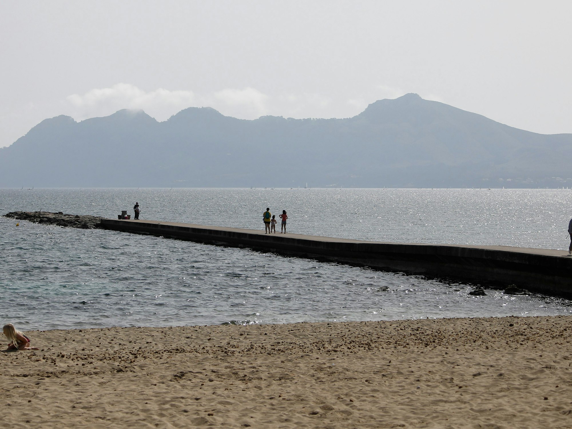 Menschen sonnen sich im Hafen von Pollença auf der Insel Mallorca.