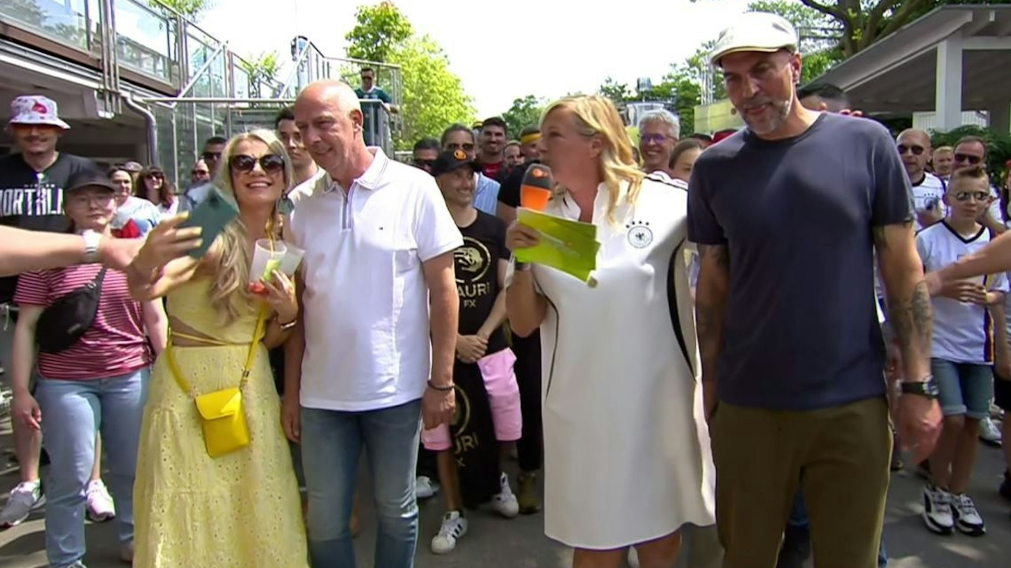 Das Foto stammt aus dem ZDF-Fernsehgarten und zeigt Markus Babbel (r.), Moderatorin Andrea Kiewel (2.v.r.) sowie Mario Basler (2.v.l.) mit einem weiblichen Fan (l.), der gerade von einem Security-Mitarbeiter am Arm gepackt wird.