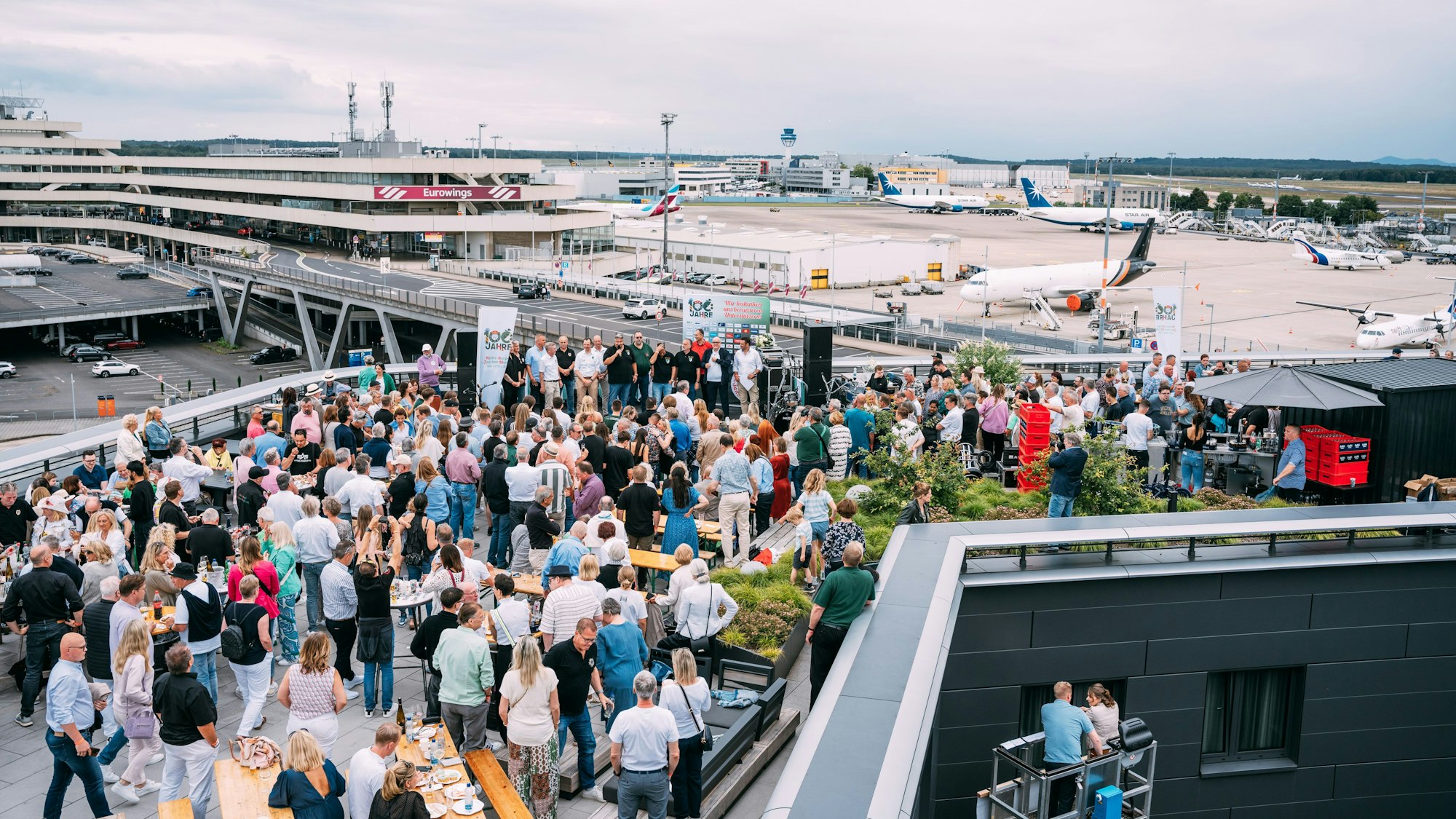 Viele Menschen auf der Dachterrassen eines Hotels am Flughafen Köln/Bonn. Im Hintergrund sind Flugzeuge zu sehen.