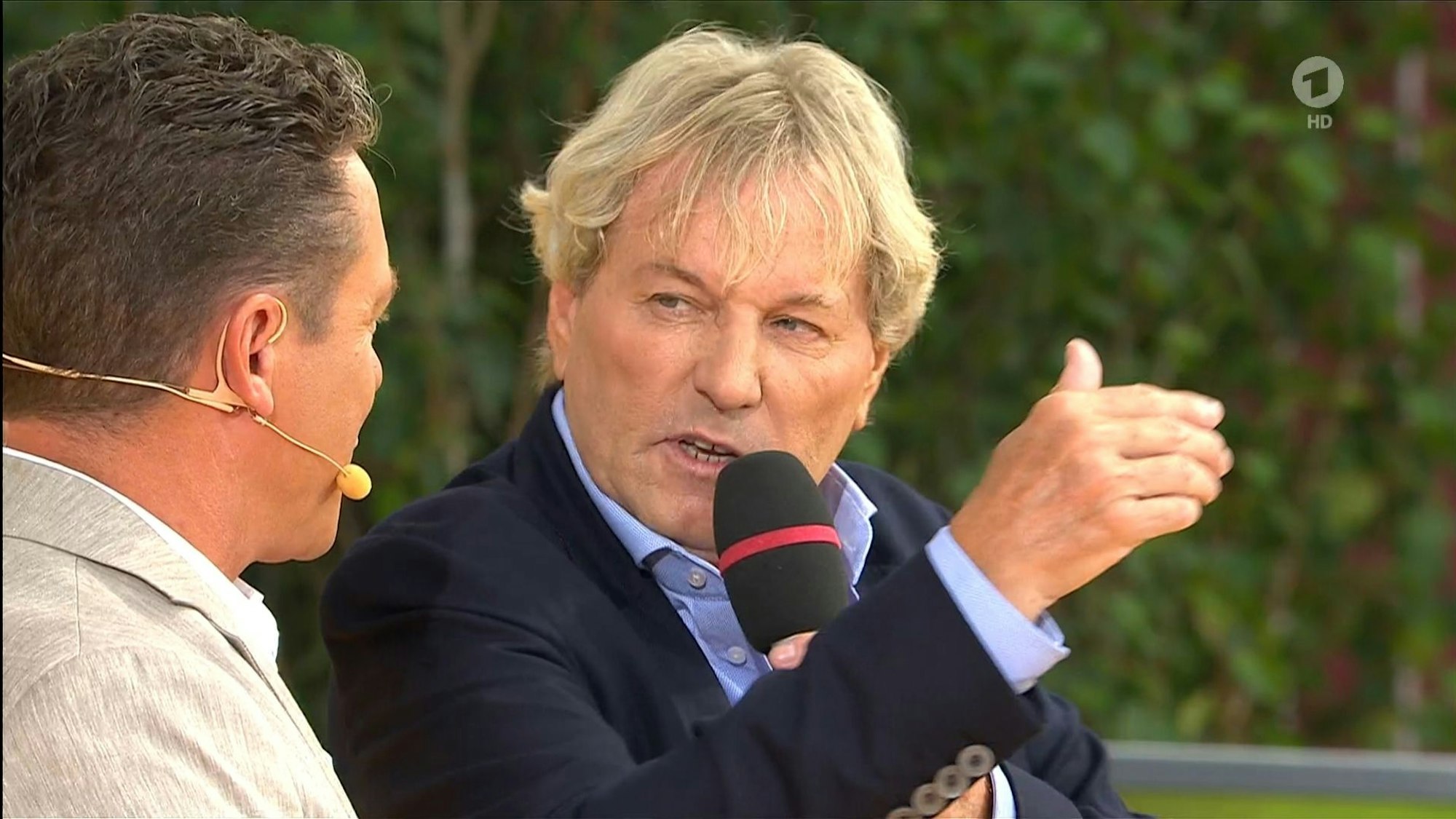 Der Screenshot stammt aus der ARD-Show Immer wieder sonntags und zeigt Moderator Stefan Mross (l.) im Gespräch mit seinem Gast Bernhard Brink (r.).