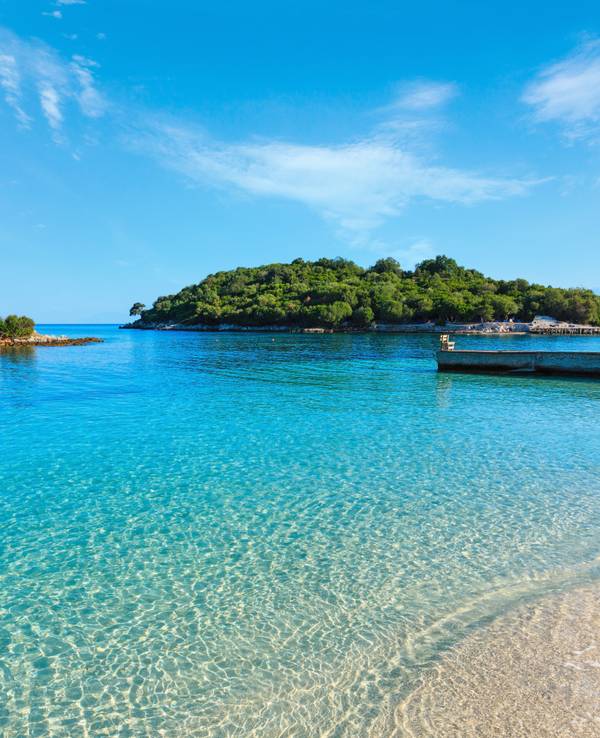 Wunderschönes Ionisches Meer mit klarem türkisfarbenem Wasser und morgendlichem Sommerblick auf die Küste vom Strand aus (Ksamil, Albanien).