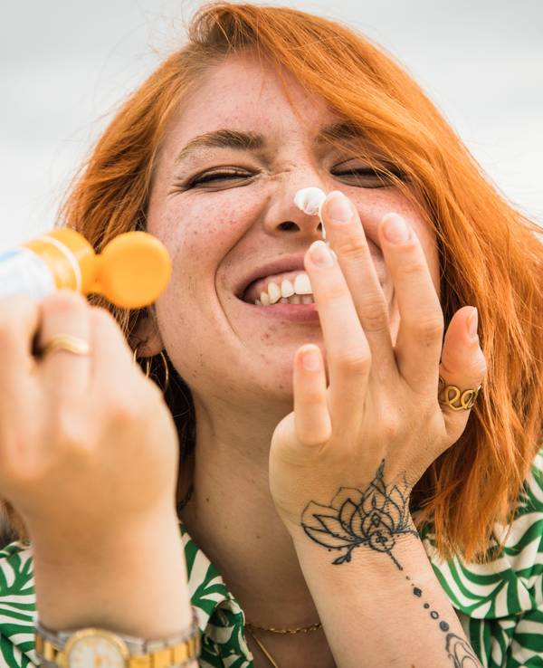 Eine junge Frau cremt sich mit kecker Miene das Gesicht ein