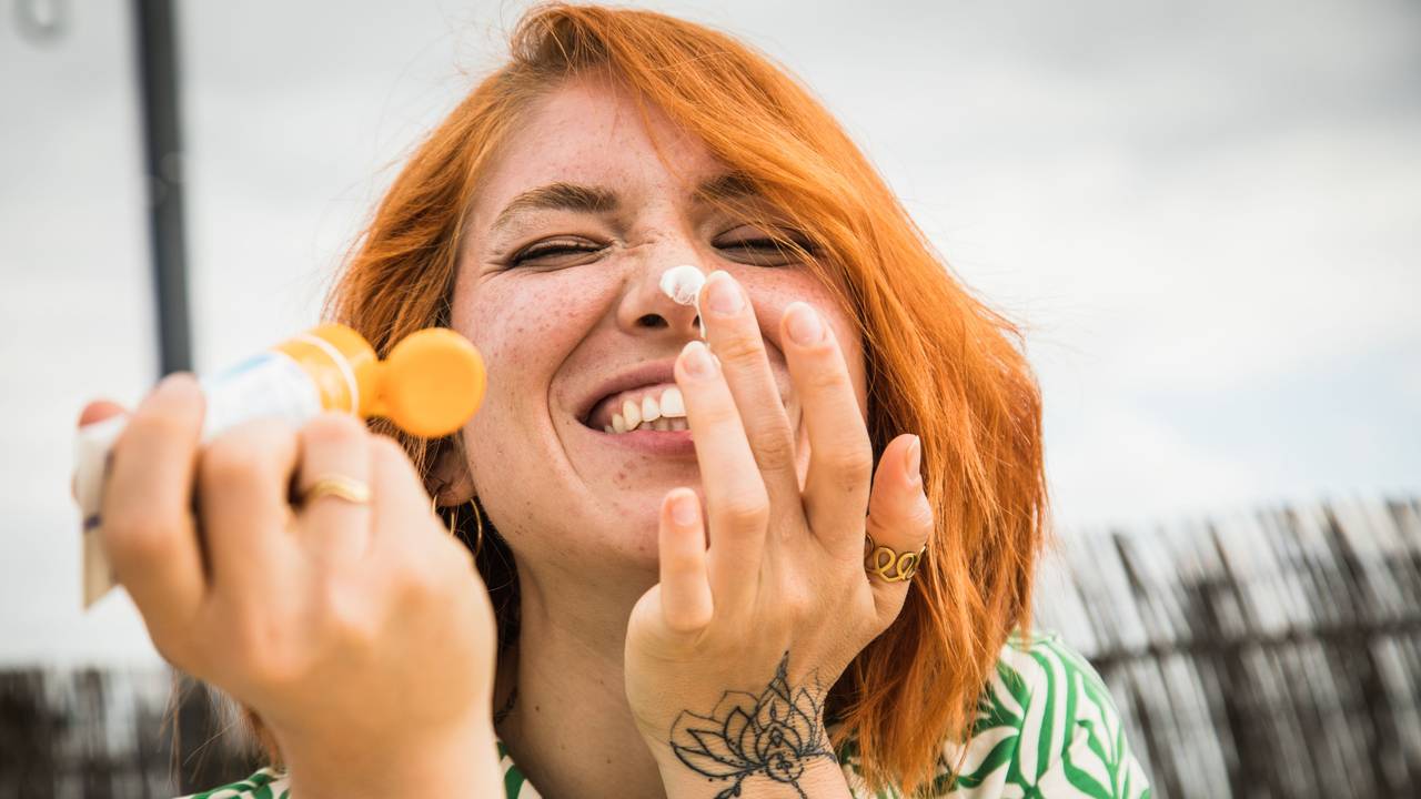 Eine junge Frau cremt sich mit kecker Miene das Gesicht ein
