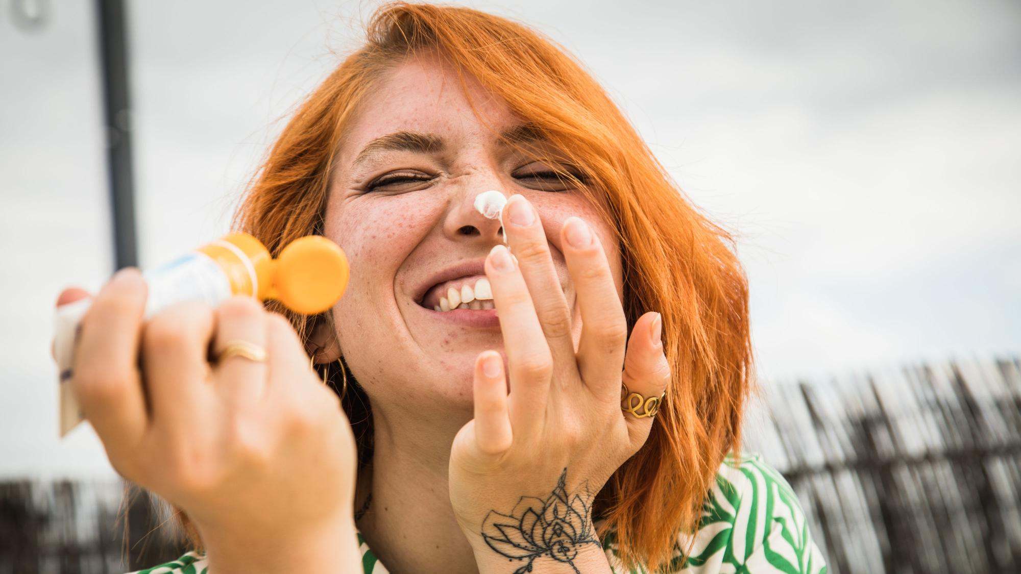Eine junge Frau cremt sich mit kecker Miene das Gesicht ein