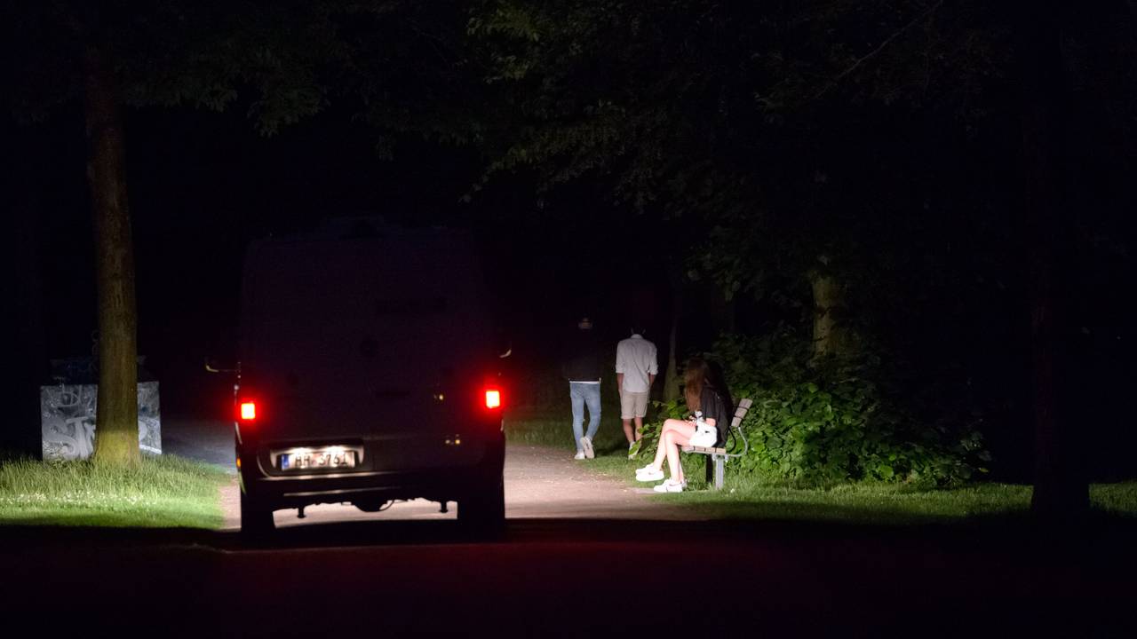 Ein Polizeifahrzeug fährt durch den dunklen, fast menschenleeren Stadtpark in Hamburg, während im Licht der Scheinwerfer vier Jugendliche stehen oder laufen.