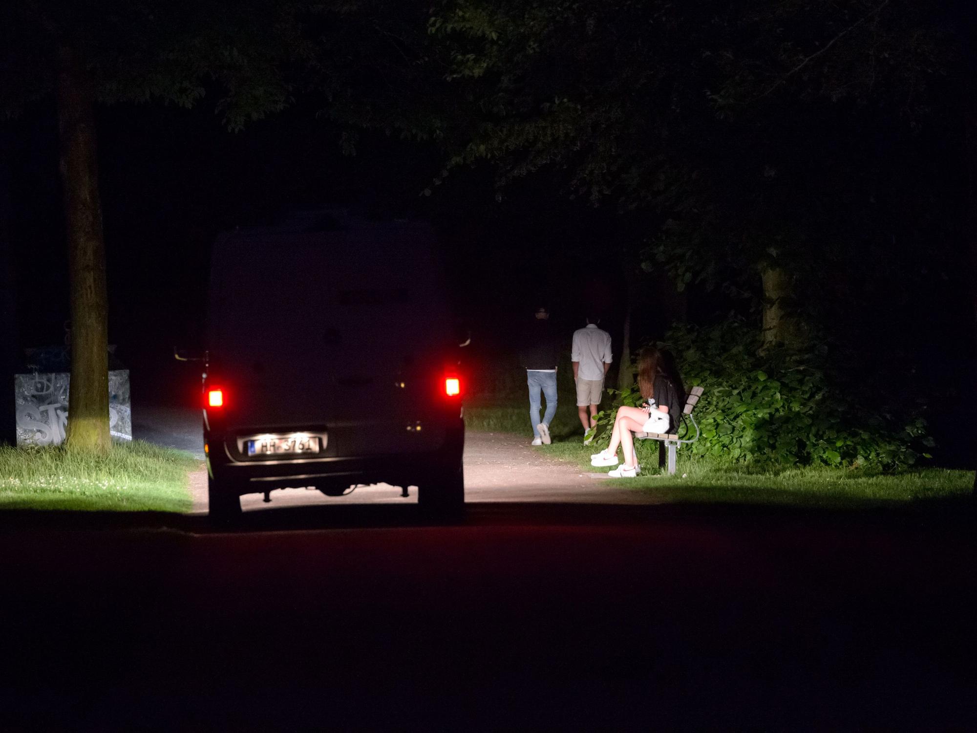 Ein Polizeifahrzeug fährt durch den dunklen, fast menschenleeren Stadtpark in Hamburg, während im Licht der Scheinwerfer vier Jugendliche stehen oder laufen.