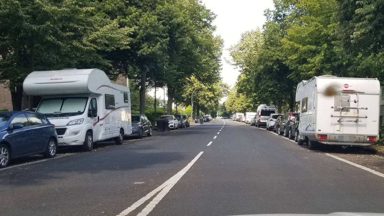 Wohnmobile und Wohnwagen parken neben Autos am Straßenrand.