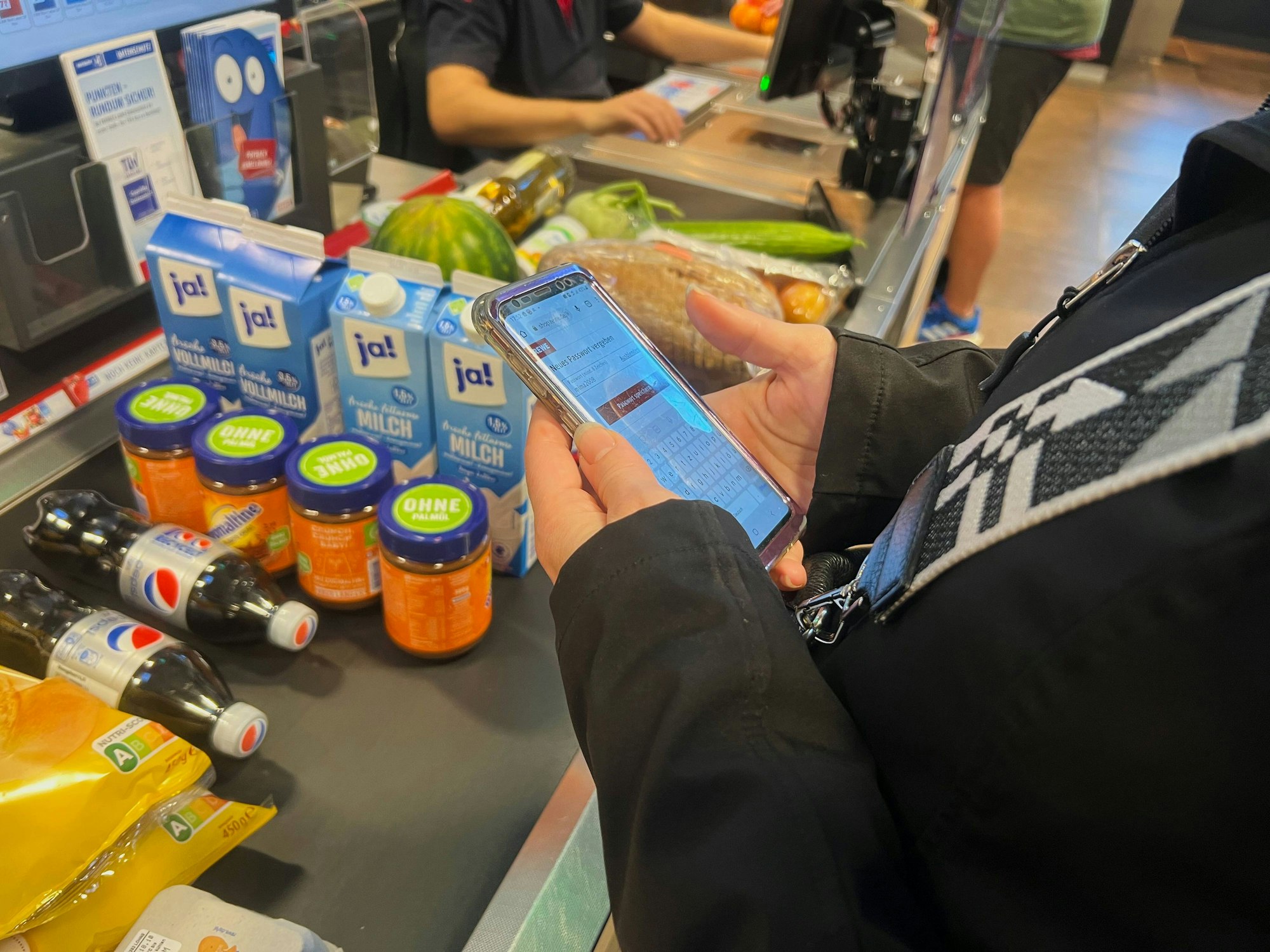 Eine Frau steht mit ihrem Handy an einer Supermarktkasse (Symbolbild): Was tun, wenn man zu wenig Bargeld dabei hat?