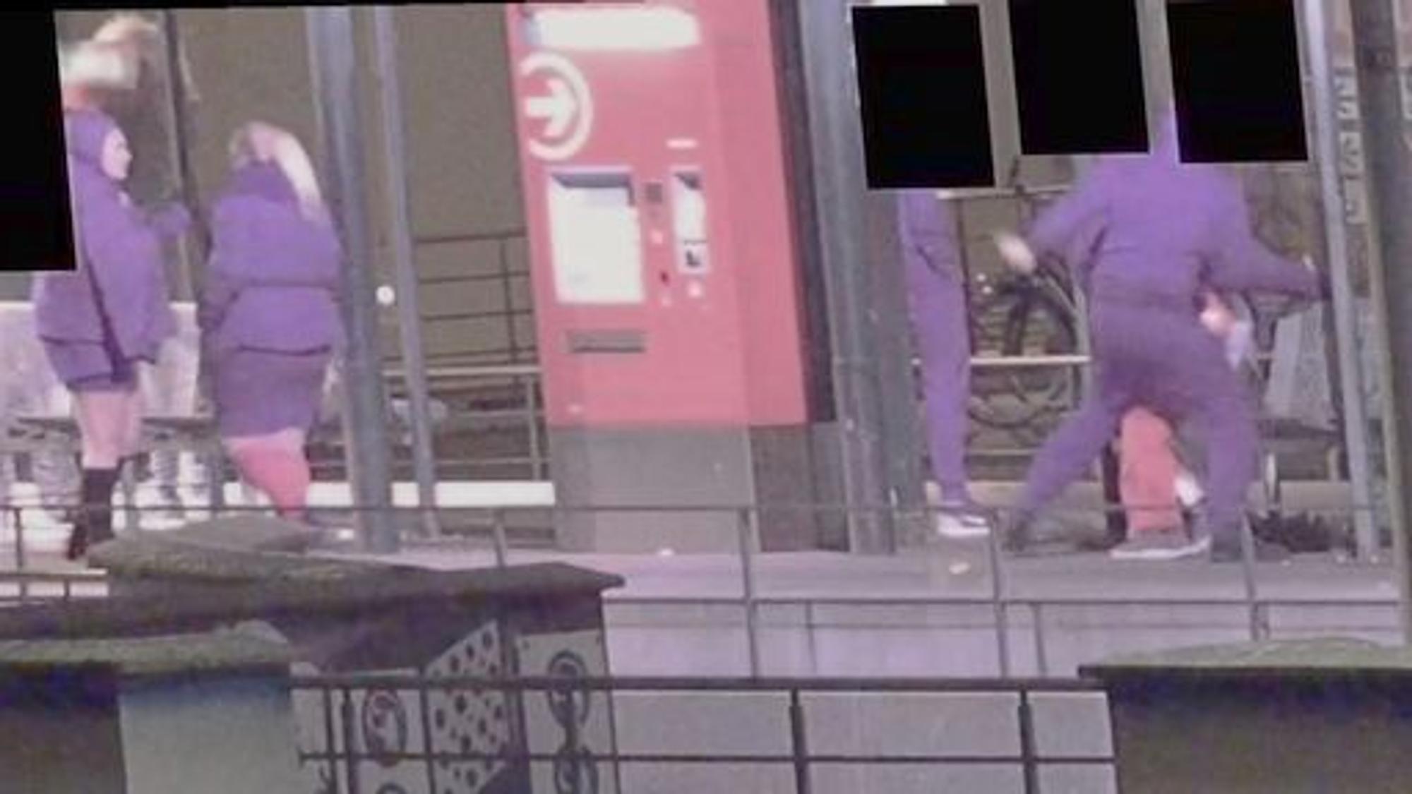 Drei Personen in violetten Outfits stehen an einer KVB-Haltestelle in Köln.