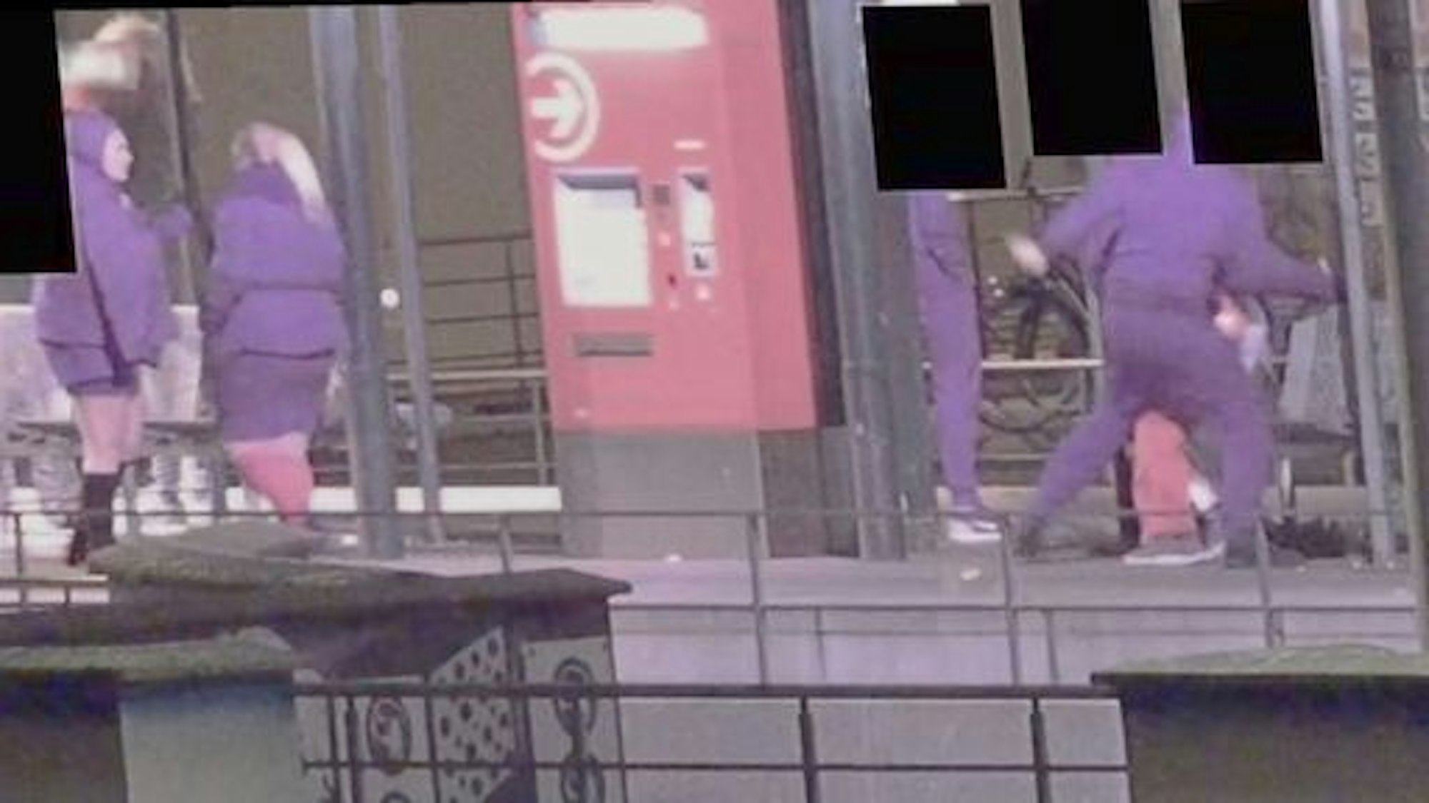 Drei Personen in violetten Outfits stehen an einer KVB-Haltestelle in Köln.