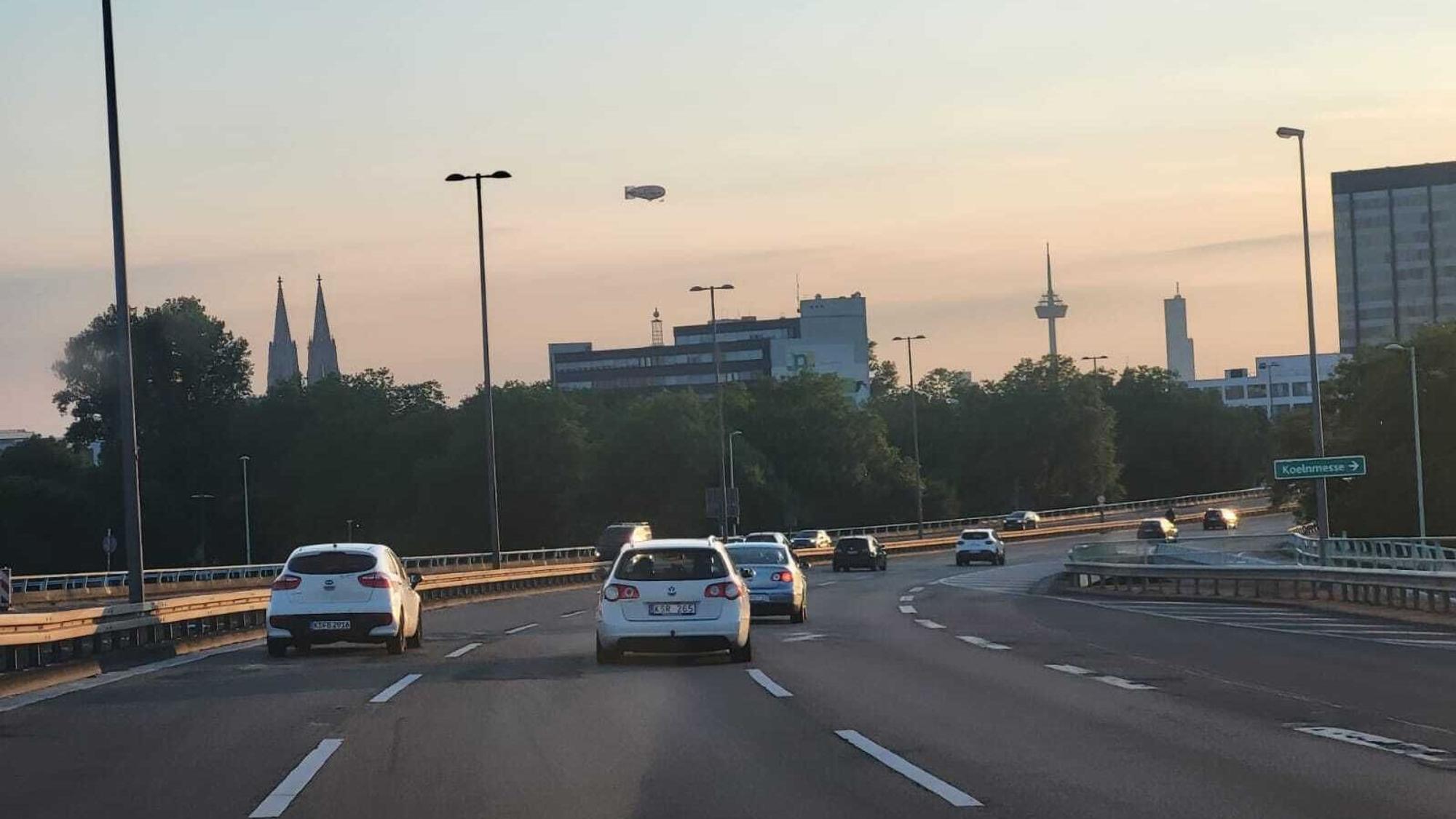 Blick von der Kölner Zoobrücke aus in den wolkenlosen Kölner Himmel, wo ein Zeppelin zu sehen ist.
