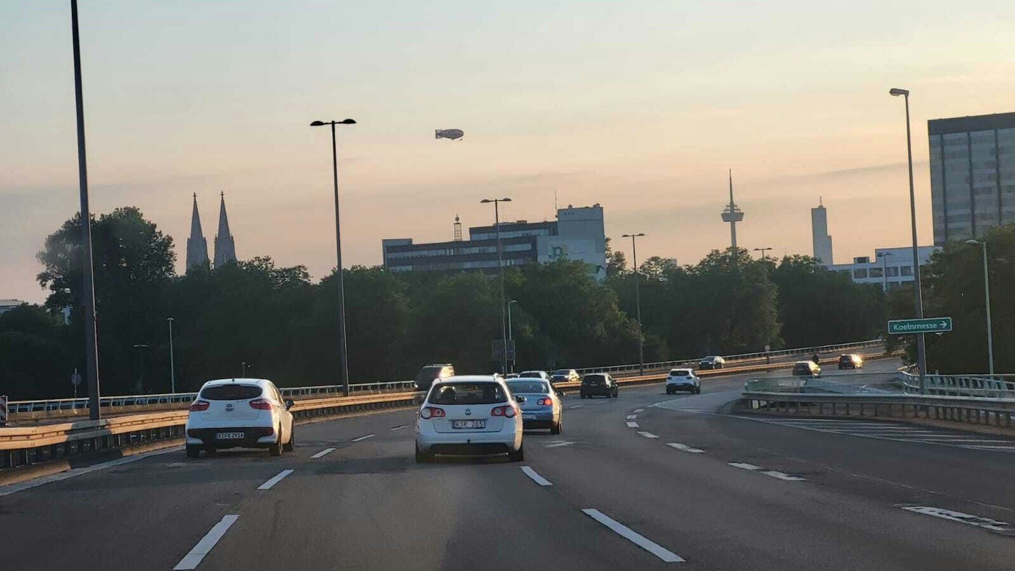 Blick von der Kölner Zoobrücke aus in den wolkenlosen Kölner Himmel, wo ein Zeppelin zu sehen ist.