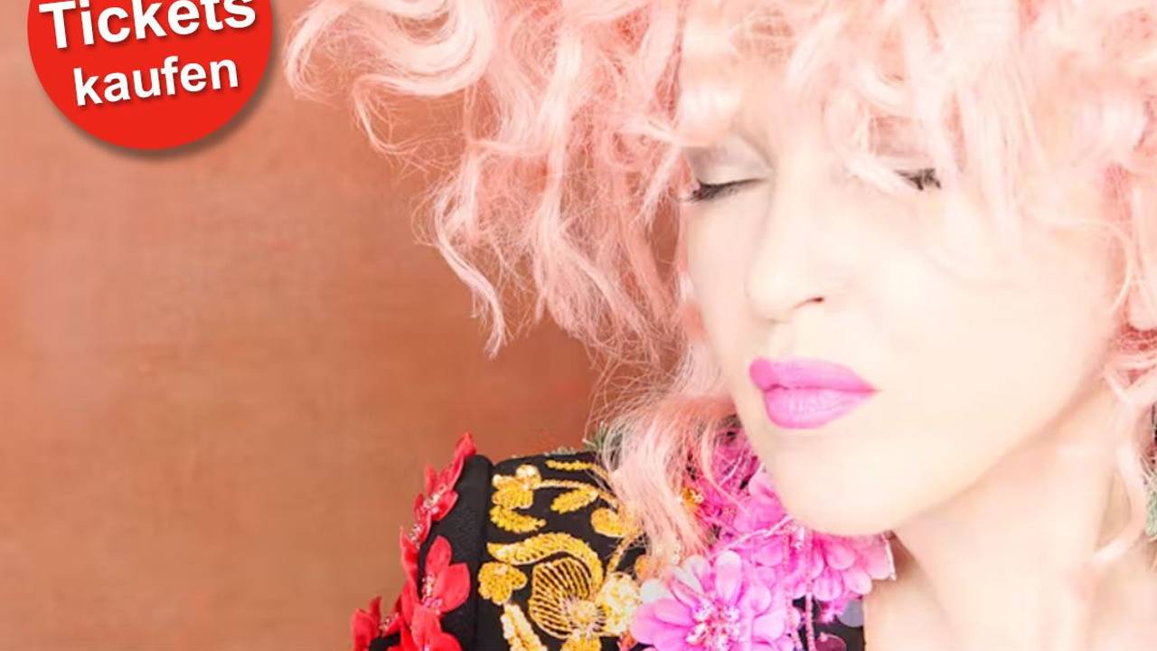 Cyndi Lauper trägt eine bunte Jacke und hat die Augen geschlossen.