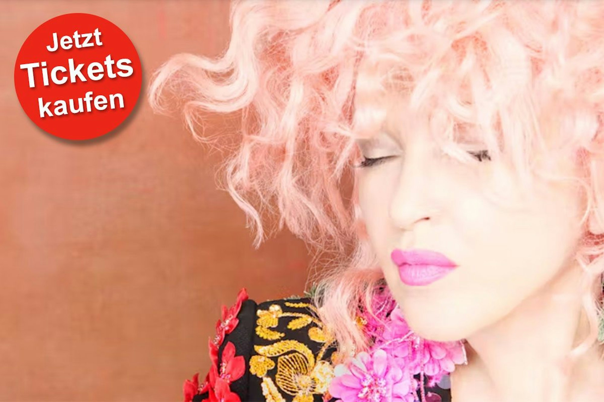 Cyndi Lauper trägt eine bunte Jacke und hat die Augen geschlossen.