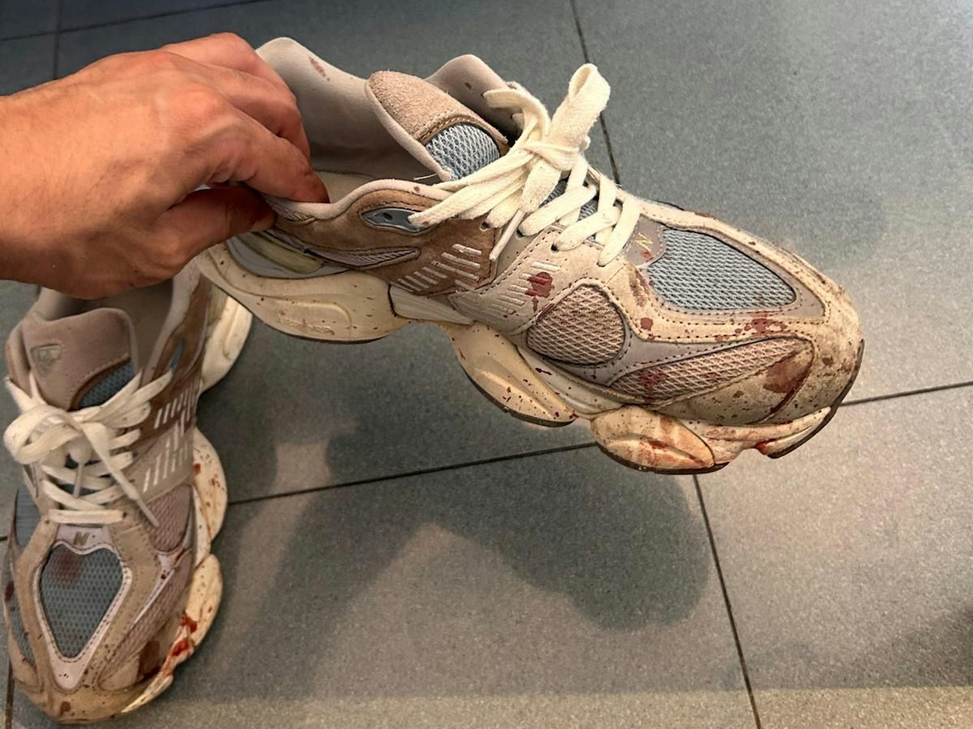 Ein Mann hält blutverschmierte Schuhe in der Hand.