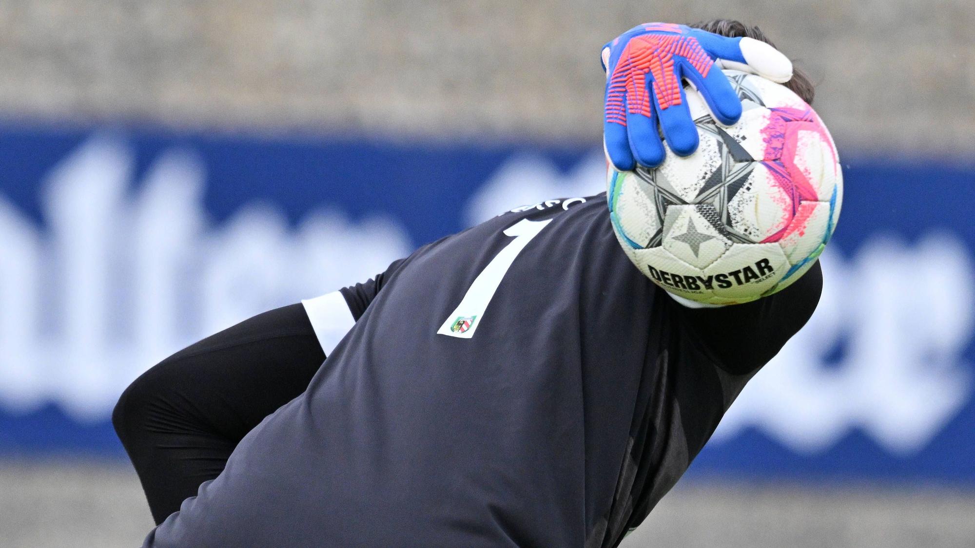 Ein Fußballtorwart hält den Ball in einer Hand.