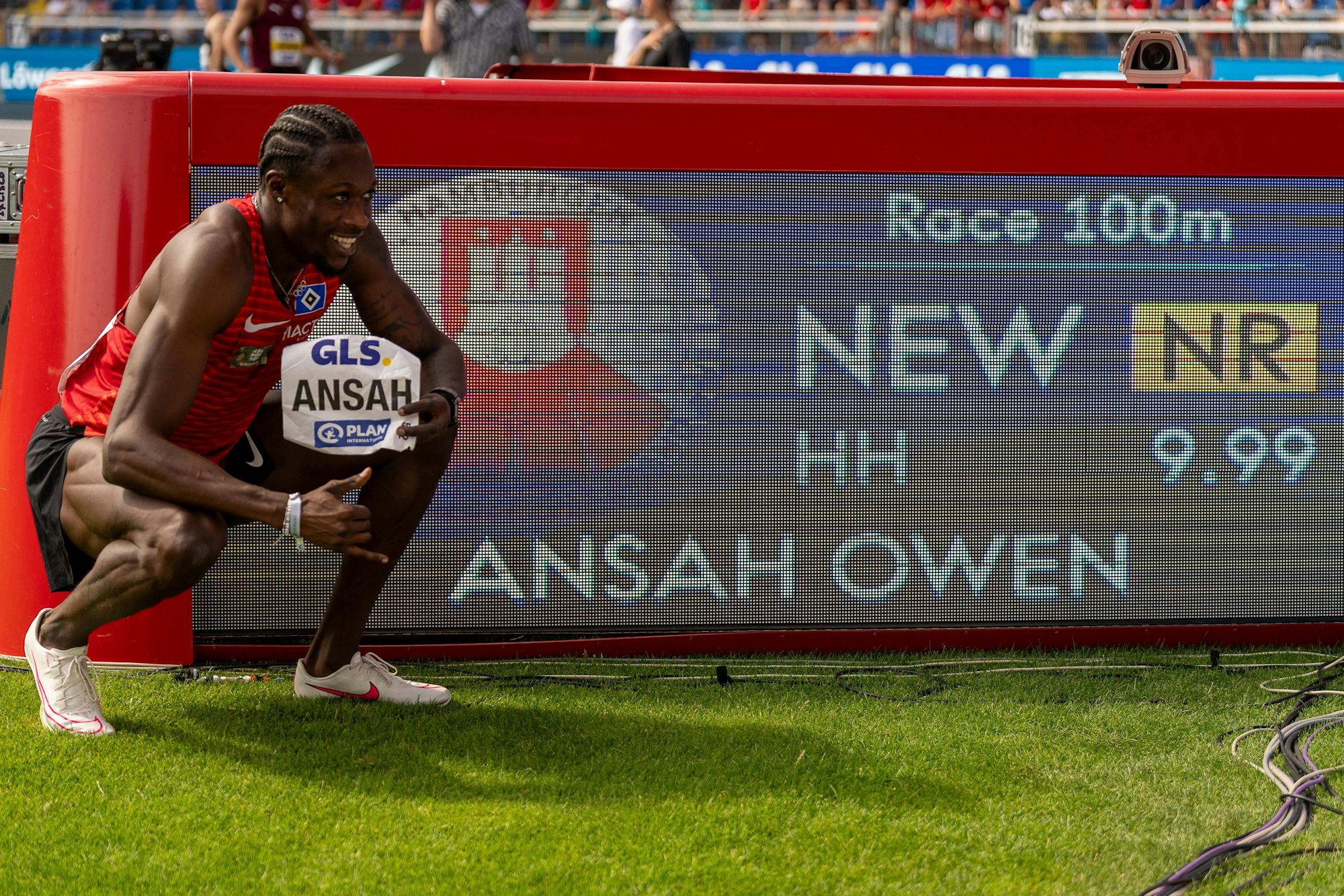 Owen Ansah hockt neben der Anzeige, die 9,99 Sekunden über 100 Meter für ihn ausweist.