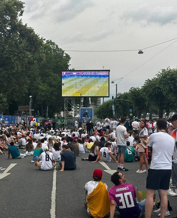 Menschen stehen beim Public Viewing auf einem Platz.