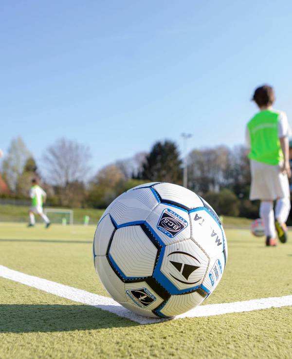 Ein Fußball liegt auf dem Eckpunkt vor spielenden Kindern.