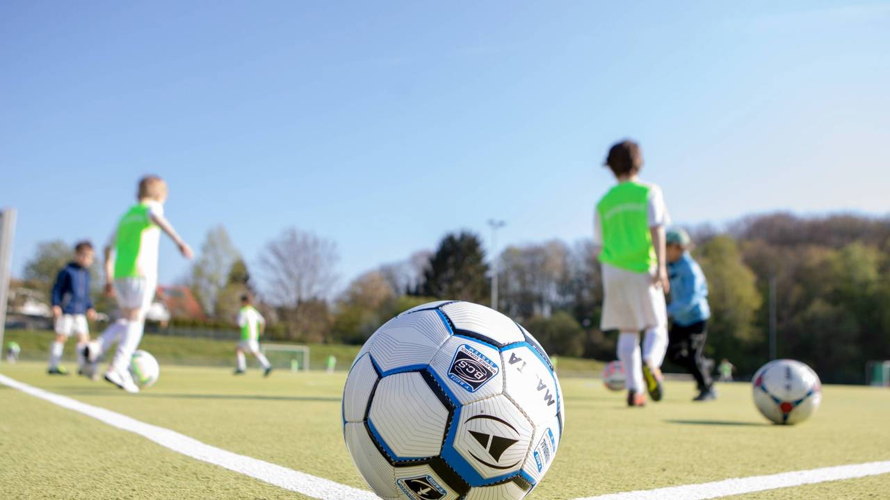 Ein Fußball liegt auf dem Eckpunkt vor spielenden Kindern.