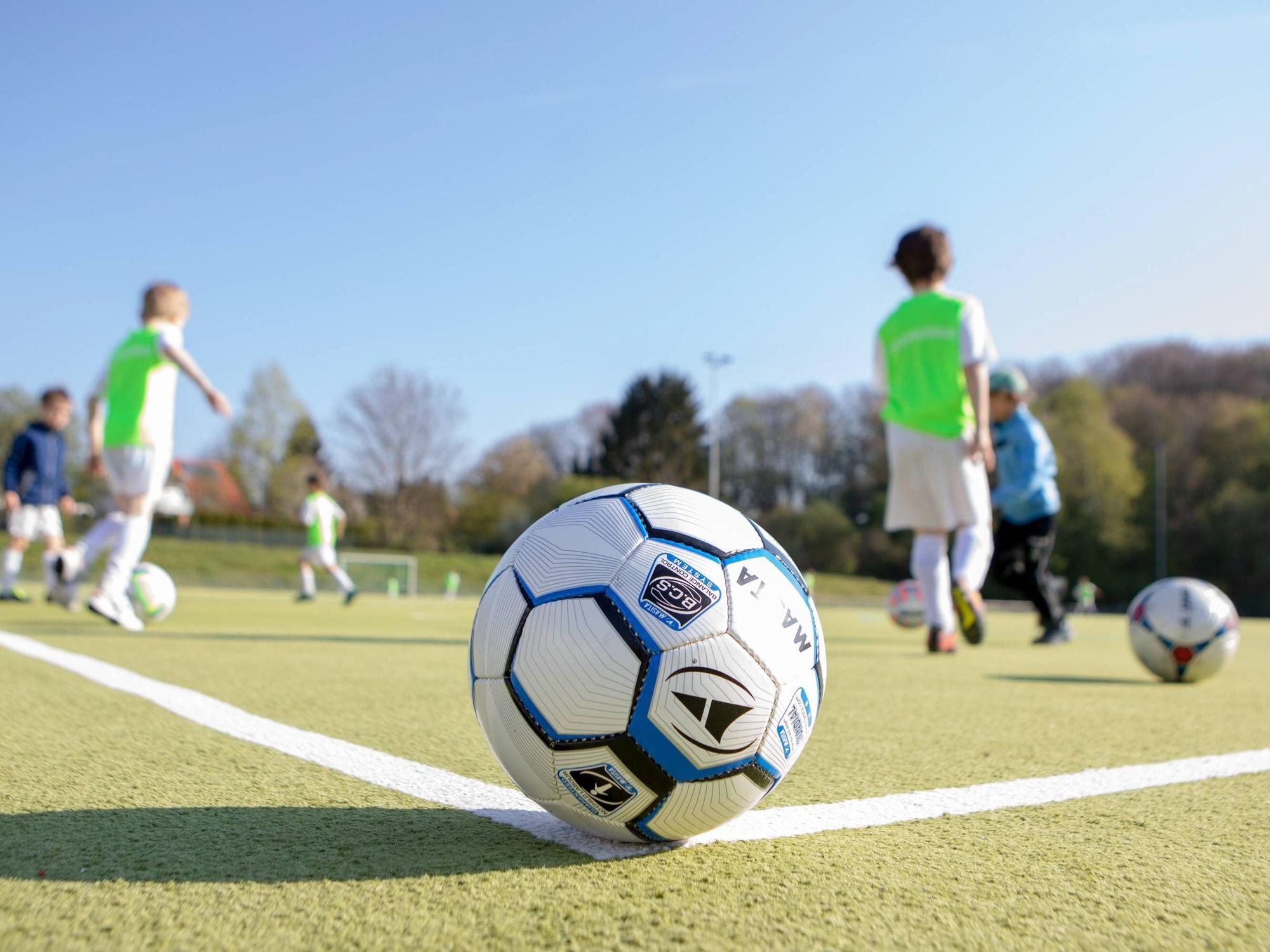 Ein Fußball liegt auf dem Eckpunkt vor spielenden Kindern.