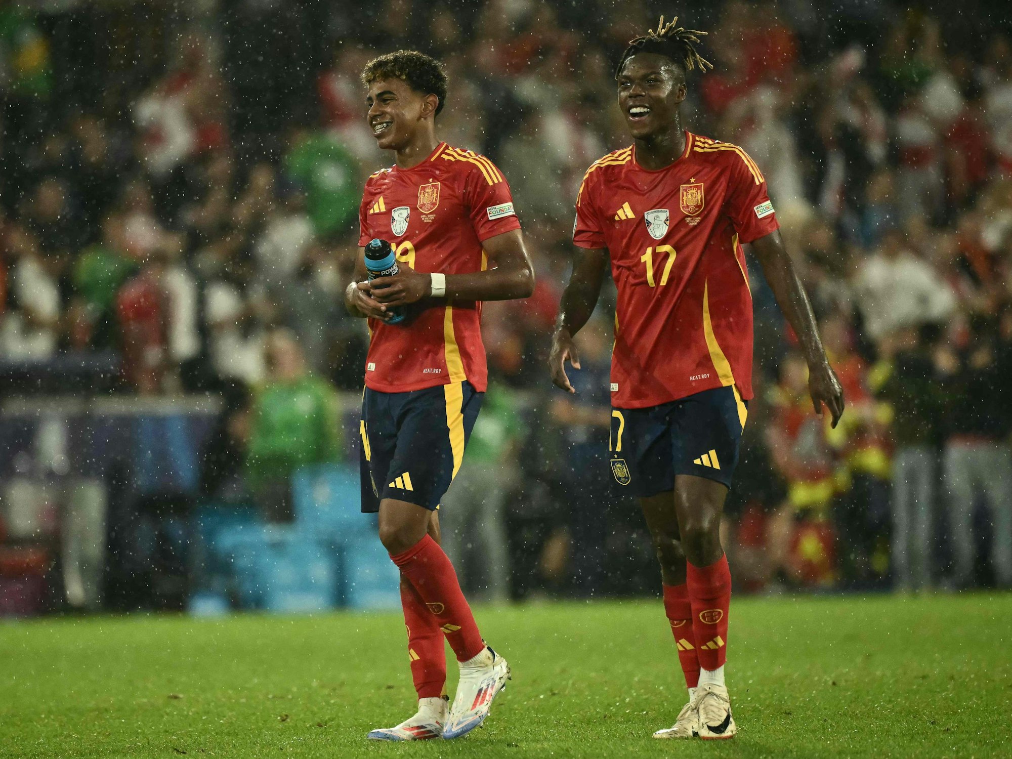 Nico Williams und Lamine Yamal lachen nach dem Spiel im Regen auf dem Spielfeld.