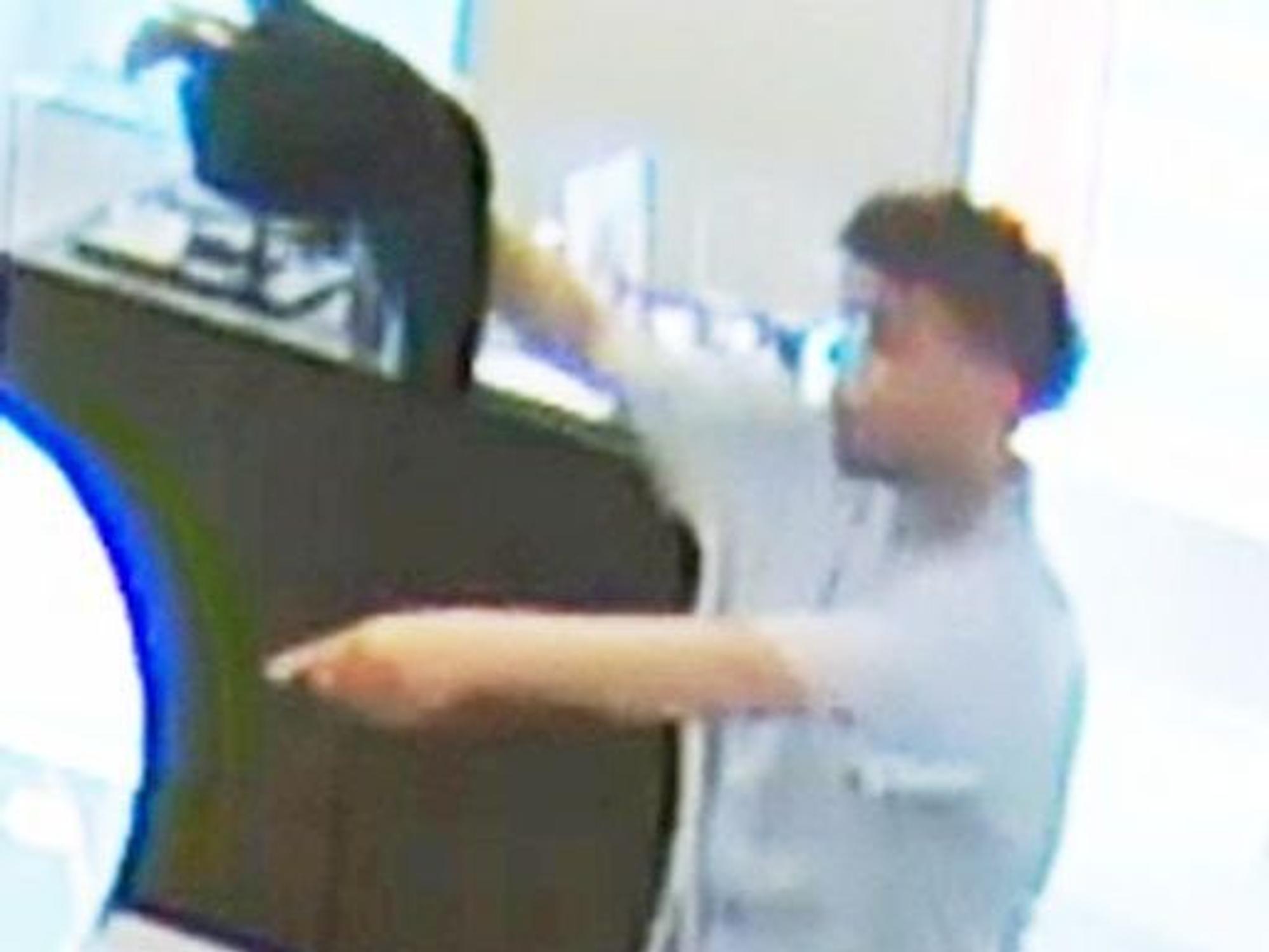 Mann mit dunklen Haaren steht bei einem Überfall bei einem Kölner Juwelier vor einer Theke und zeigt auf Gegenstände.