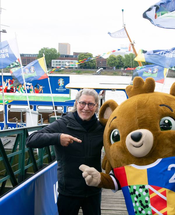 Toni Schumacher legt seinen Arm und Maskottchen Albärt.