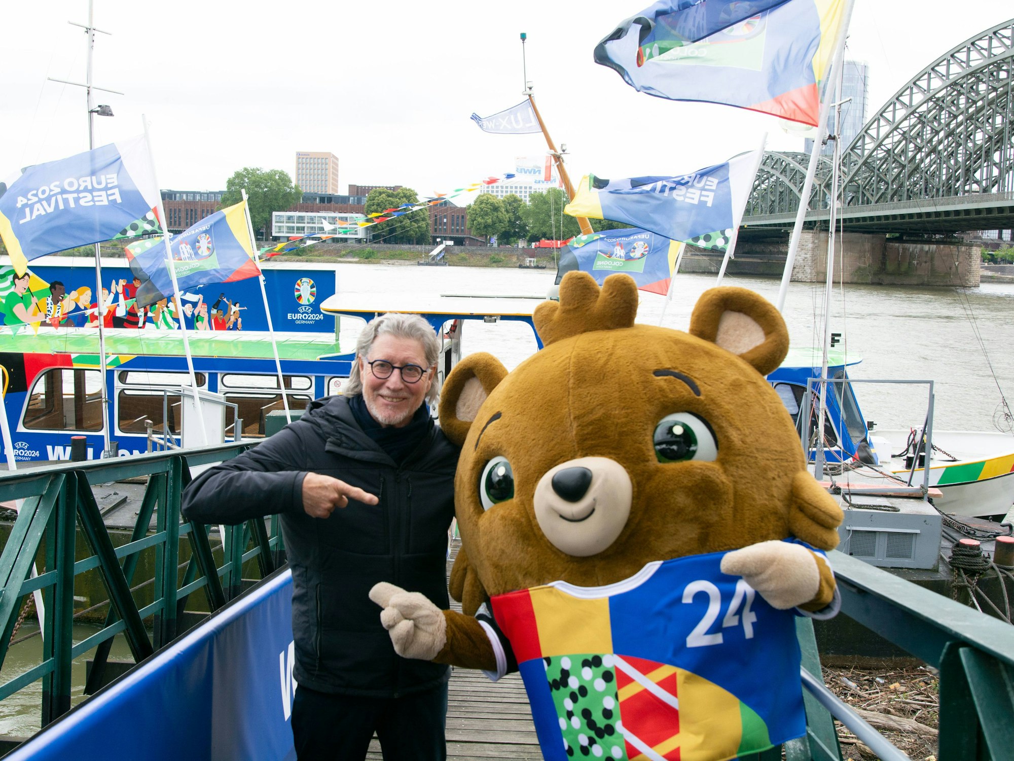 Toni Schumacher legt seinen Arm und Maskottchen Albärt.