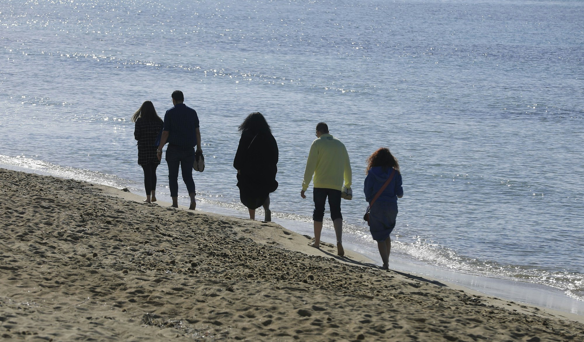 Menschen spazieren bei sonnigem Wetter am Strand von Arenal entlang.
